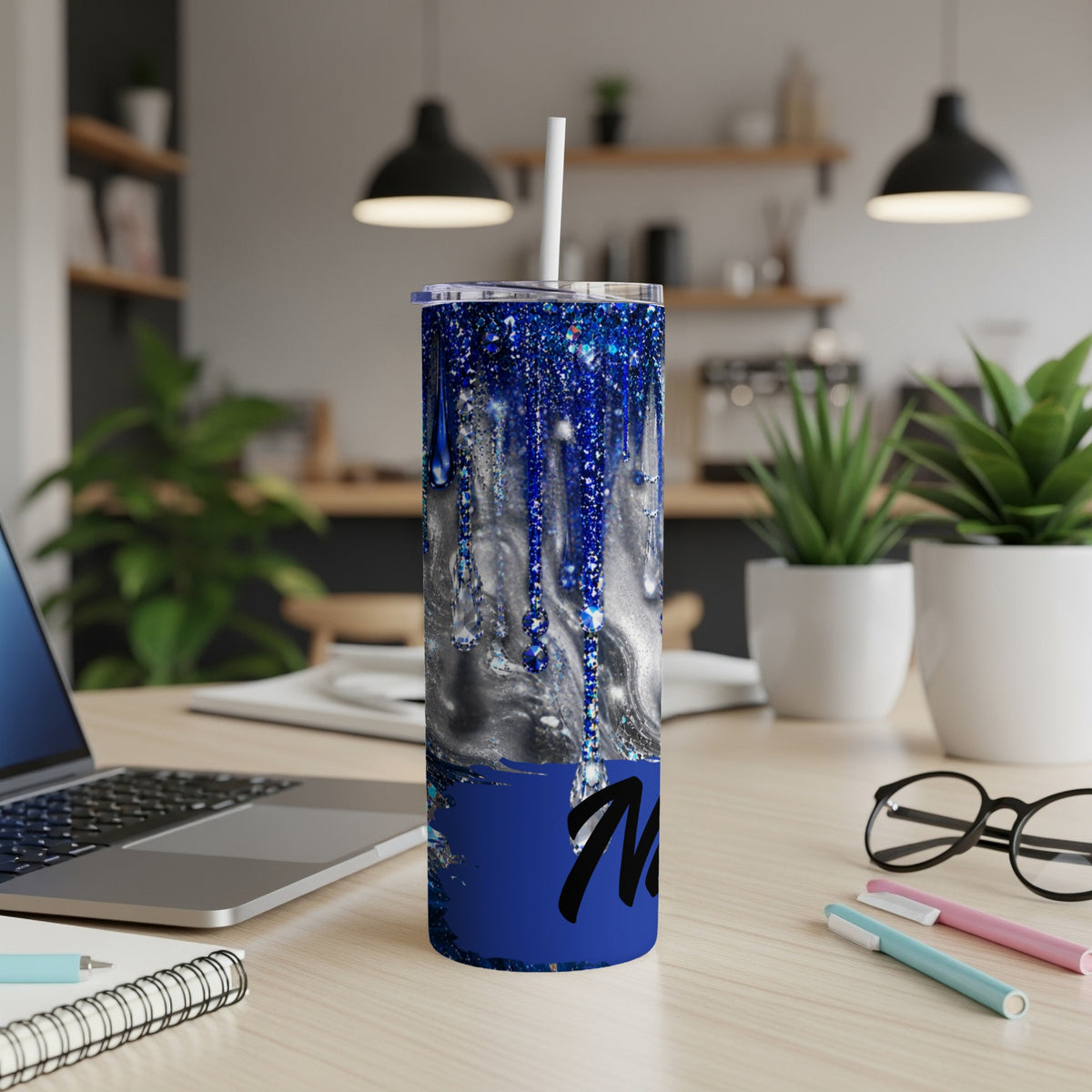 Blue glitter drip tumbler with black script "M" on a desk.