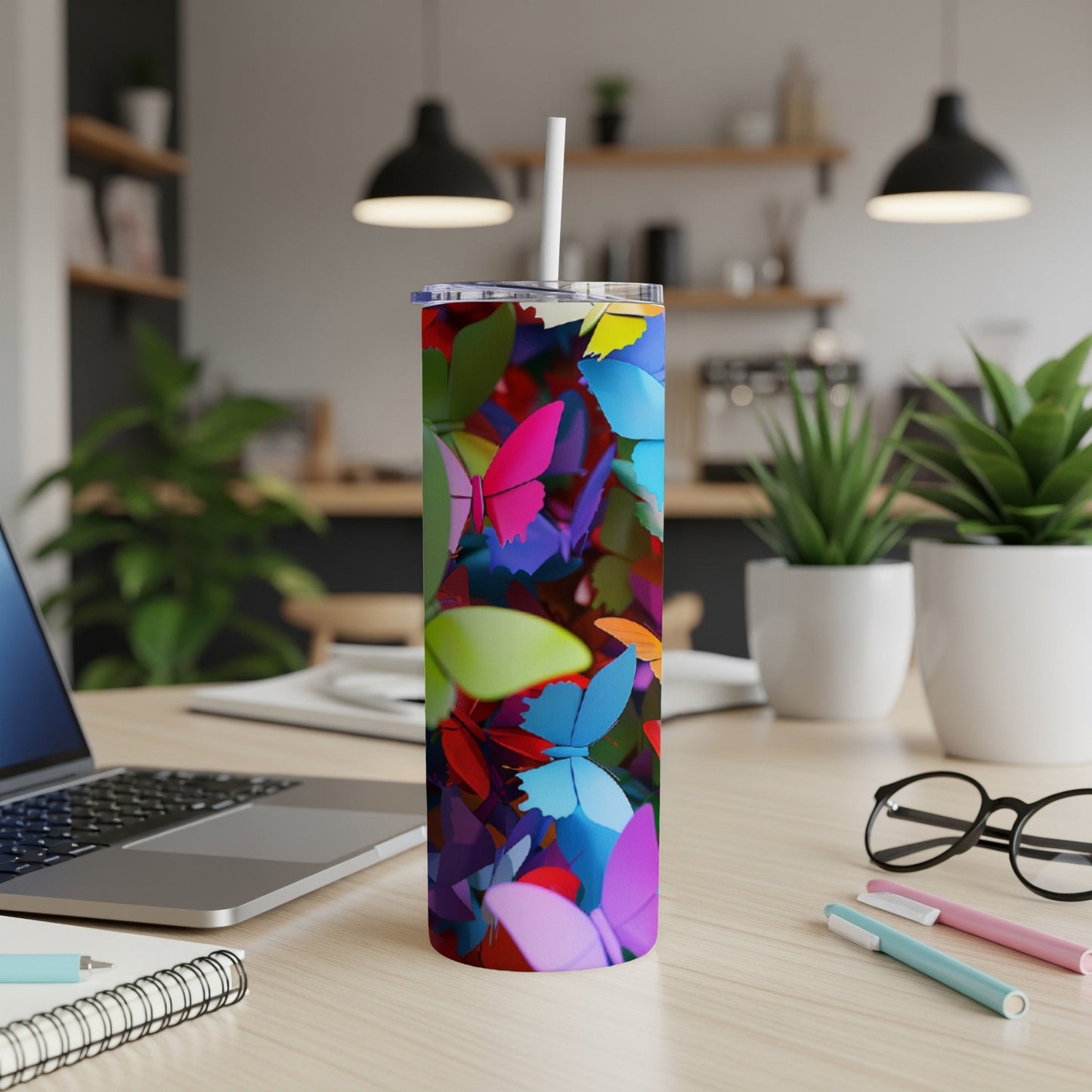 Tumbler with colorful butterflies, on a desk with a laptop and pens.