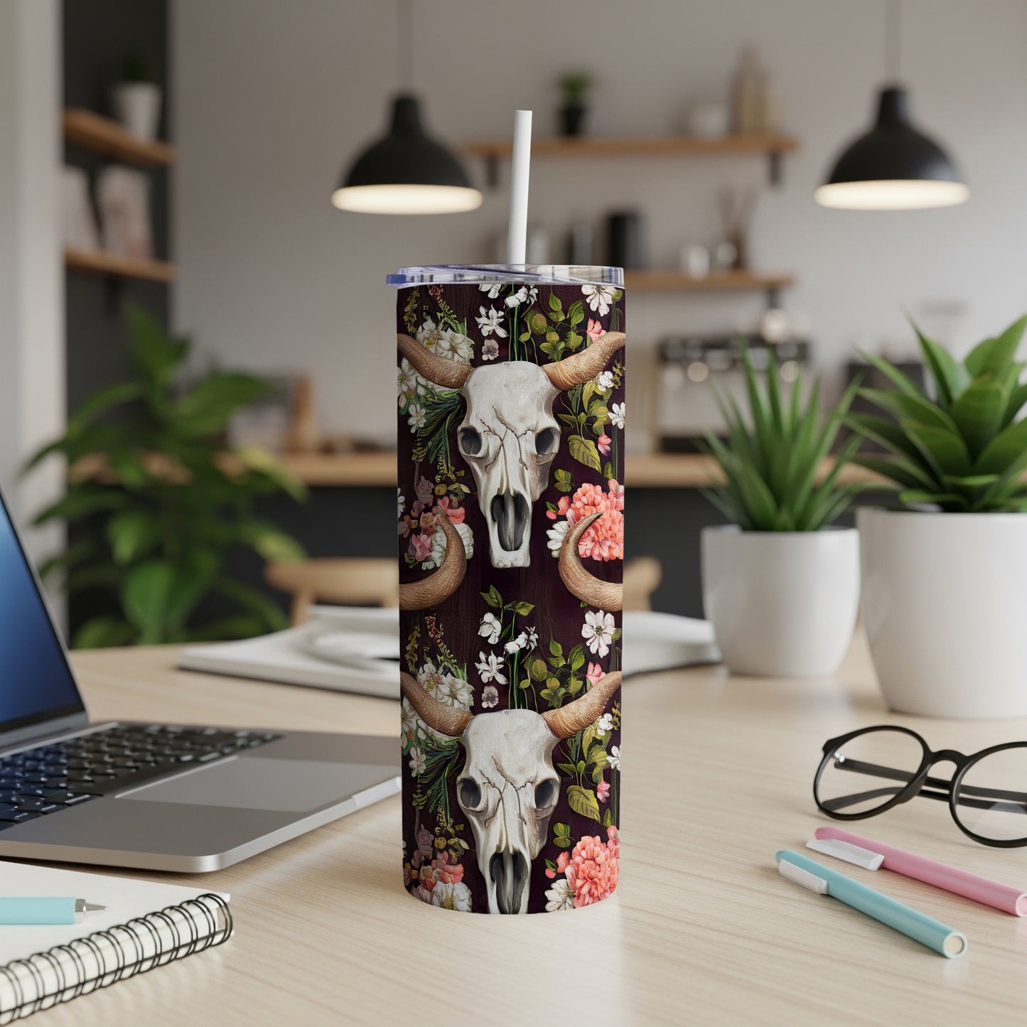 Tall tumbler with bull skull and floral design, resting on a wooden desk.