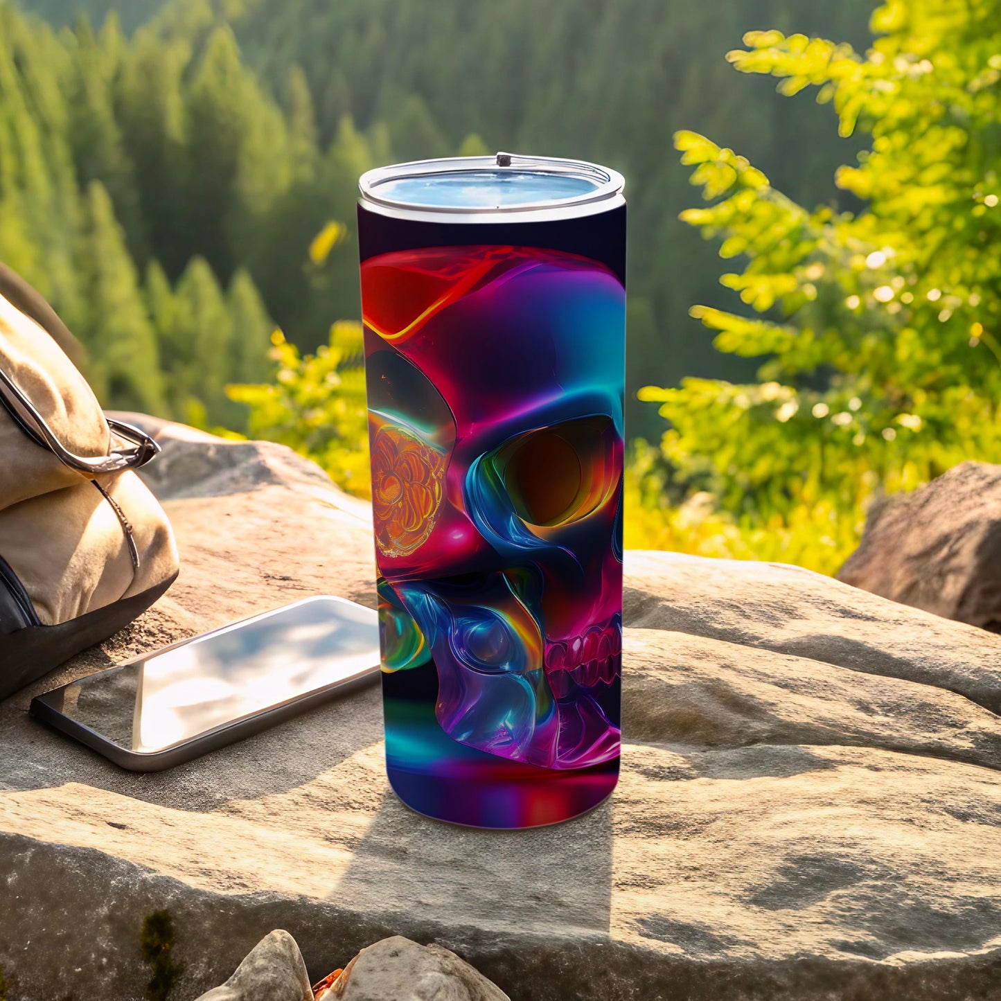 Colorful abstract skull tumbler on rocks with phone and backpack outdoors.