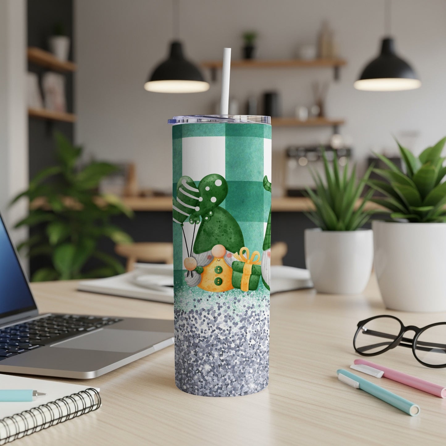 Green plaid tumbler with gnomes, balloons, and glitter on a desk.