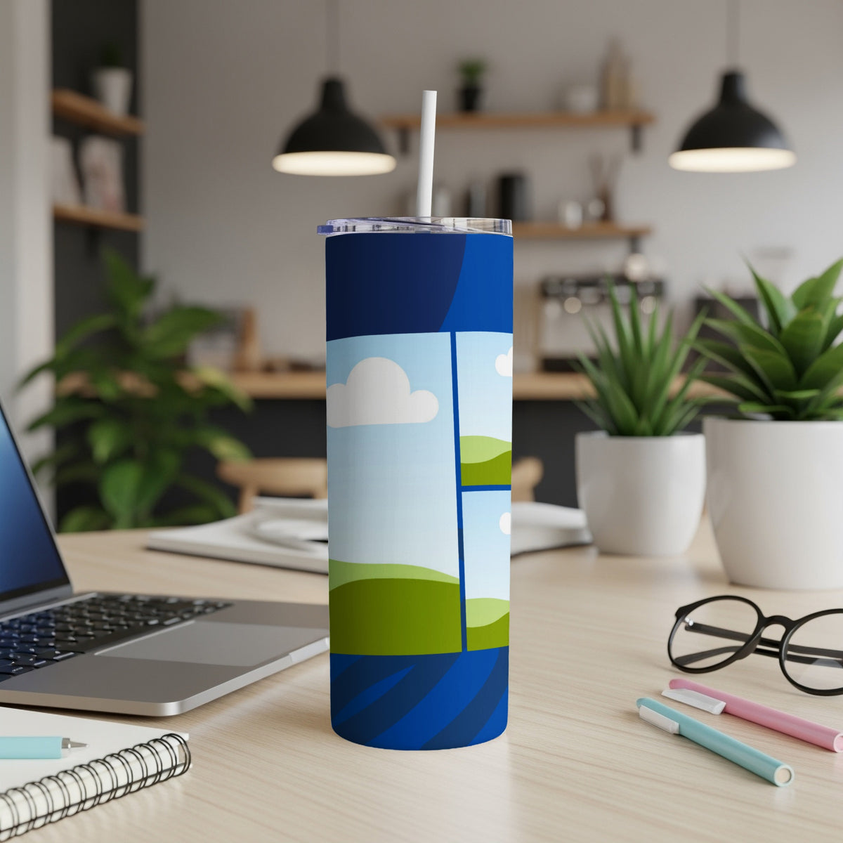Blue tumbler with cartoon landscape design on desk with laptop and glasses.