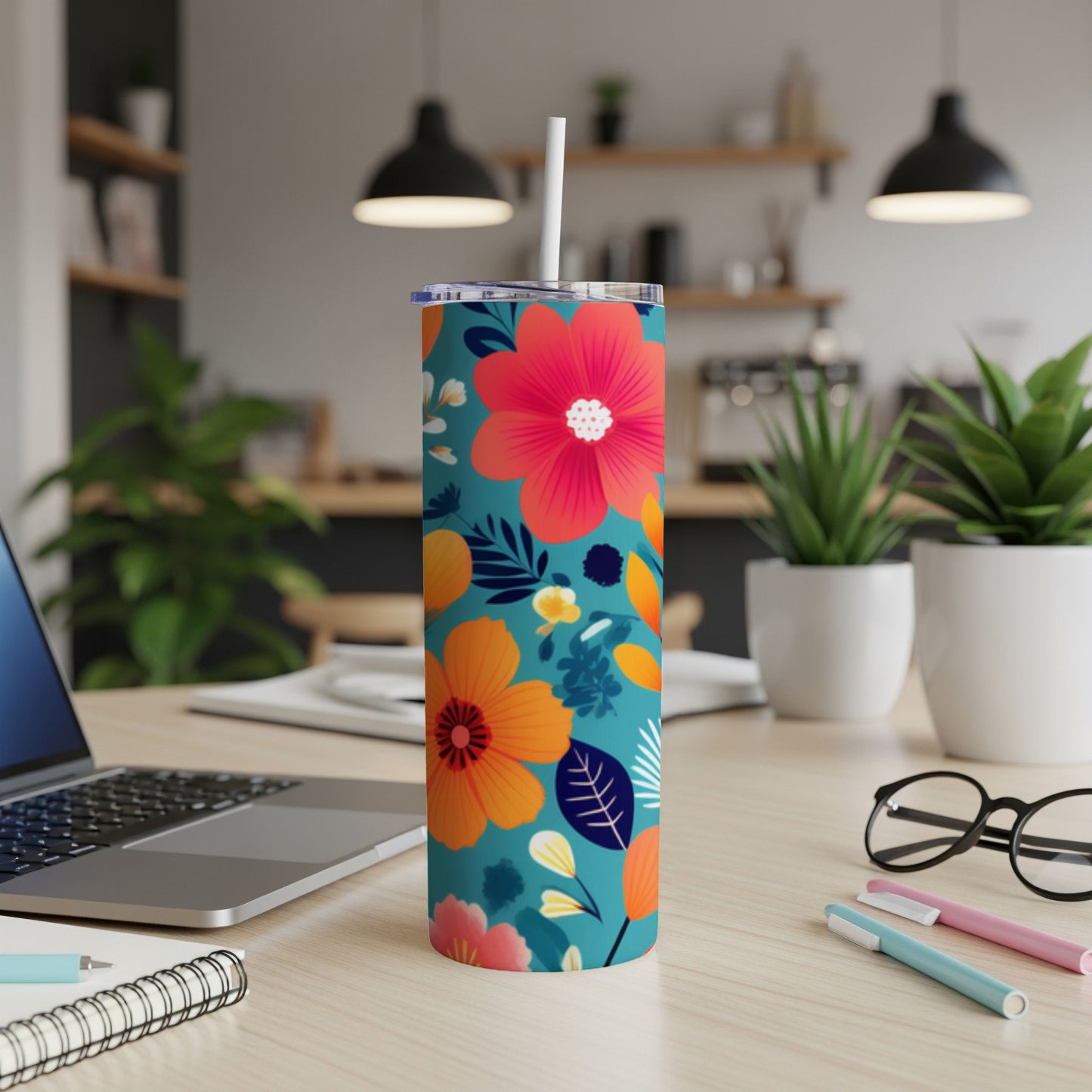 Teal tumbler with orange and pink floral pattern, on desk with laptop.
