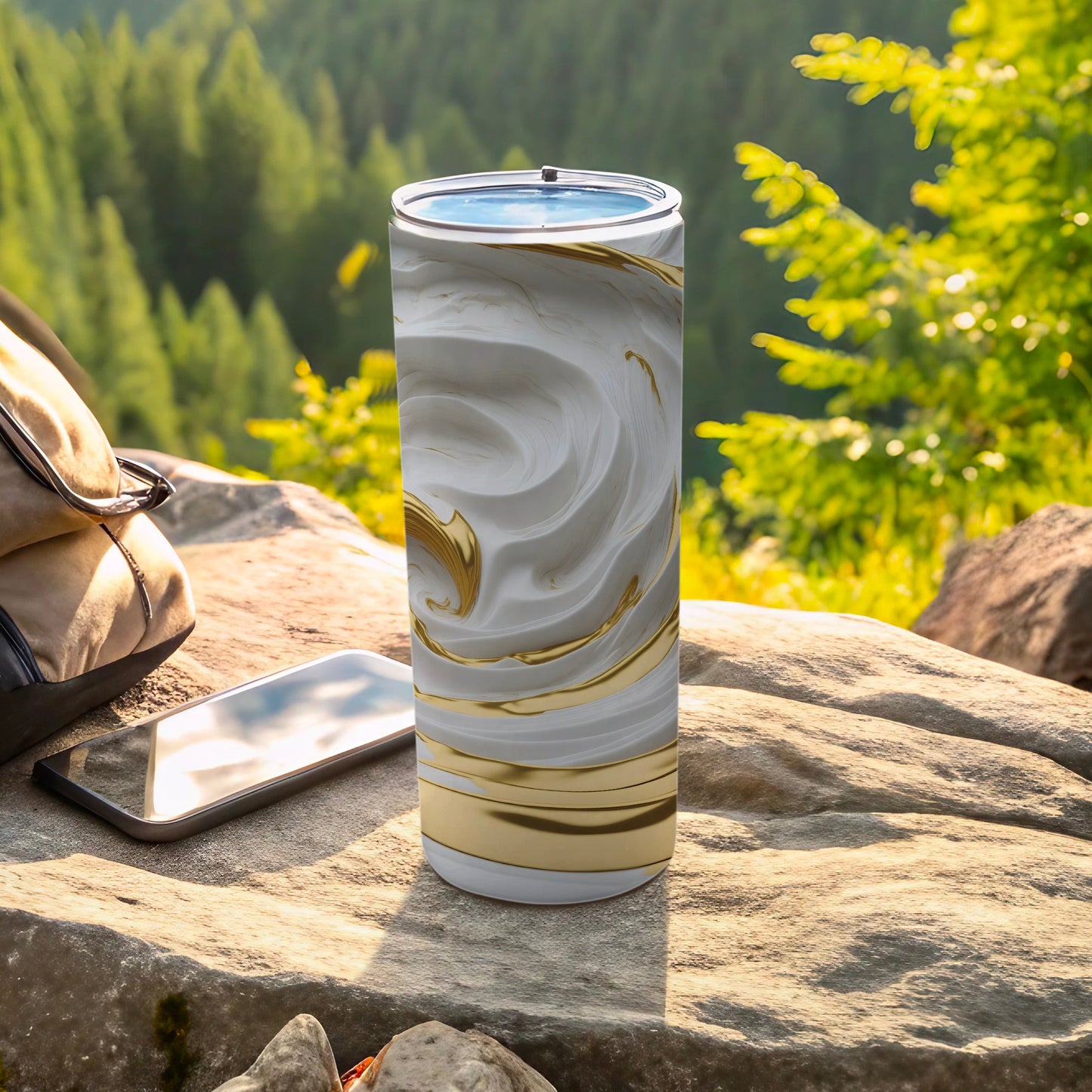White and gold marble tumbler on a rock with a phone and backpack.