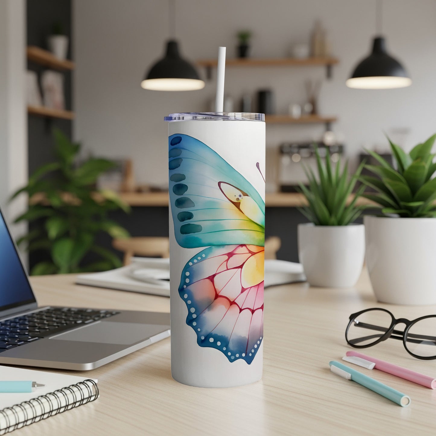 White tumbler with colorful butterfly design and straw, on a desk.