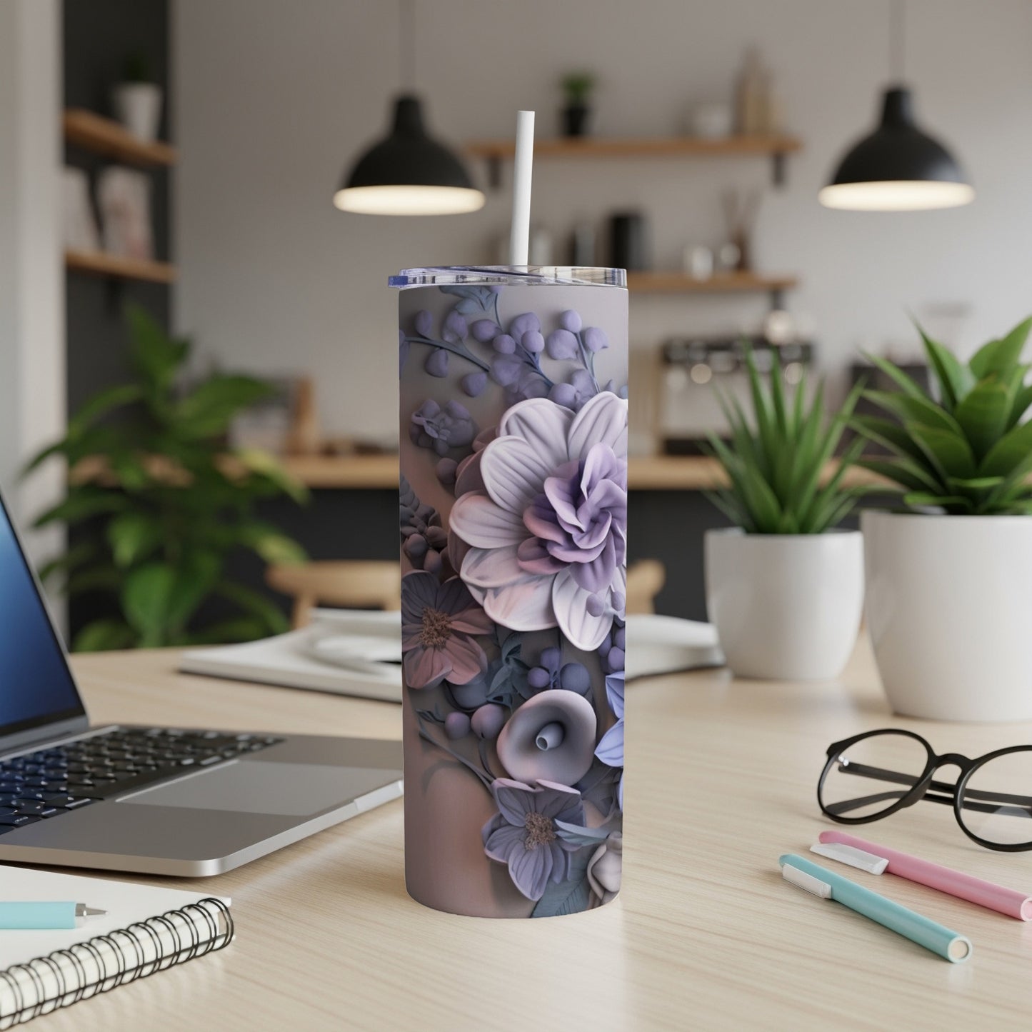 Floral tumbler with straw on a desk with a laptop and pens.