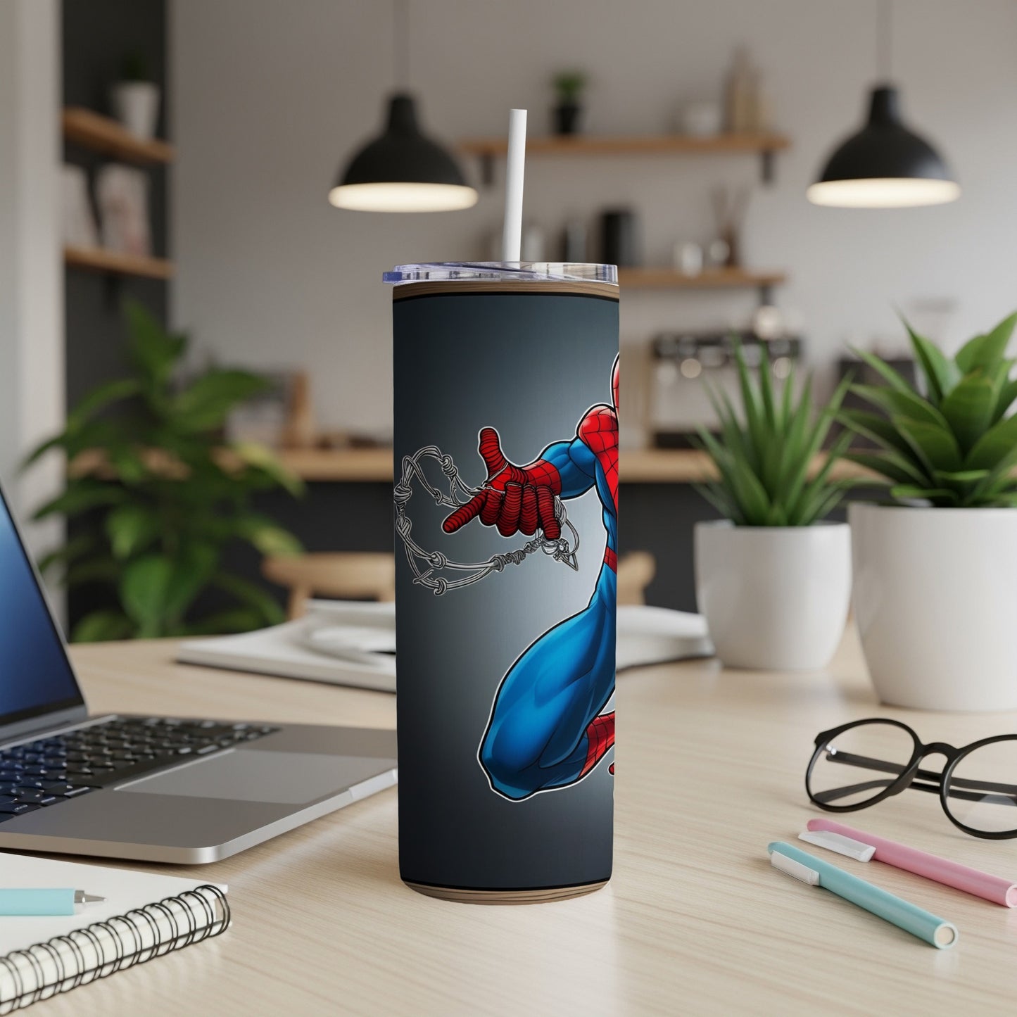 Spider-Man mid-swing on a dark gray tumbler with straw, set on a desk.