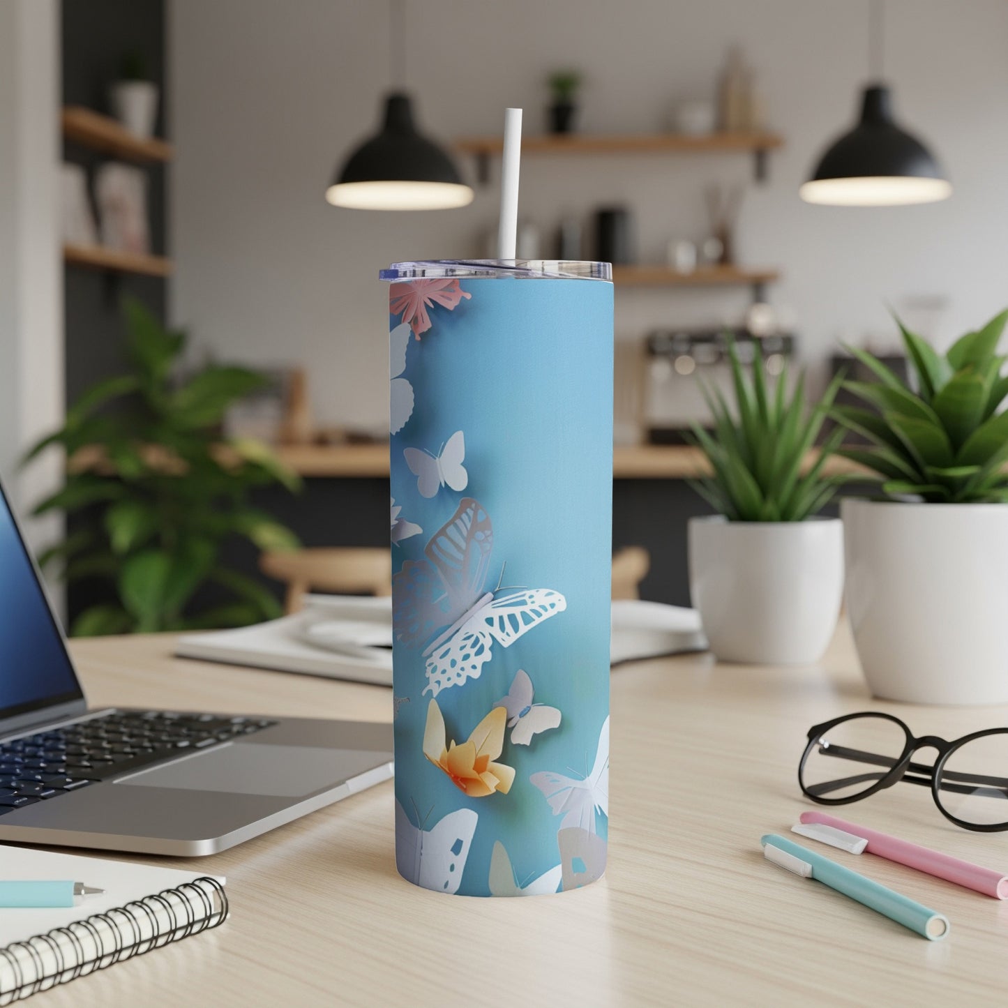 Blue tumbler with paper butterflies and a straw on a desk.