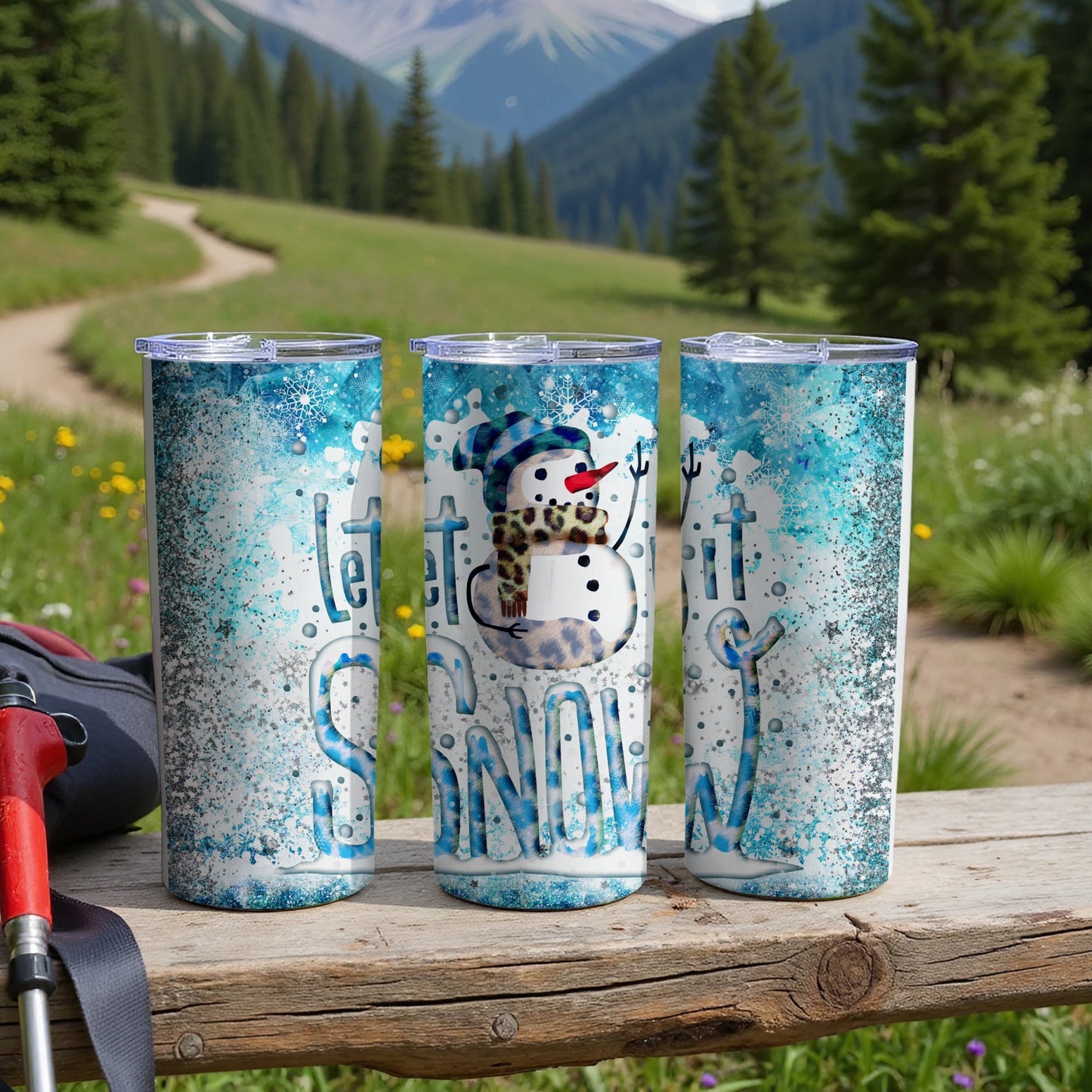 Snowman and "Let it Snow" text on three glittery blue tumblers outdoors.