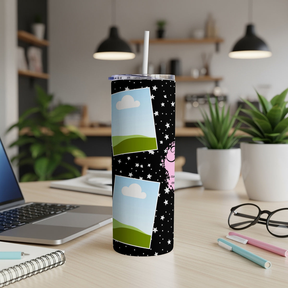 Black tumbler with stars, clouds, and pink text on a desk.