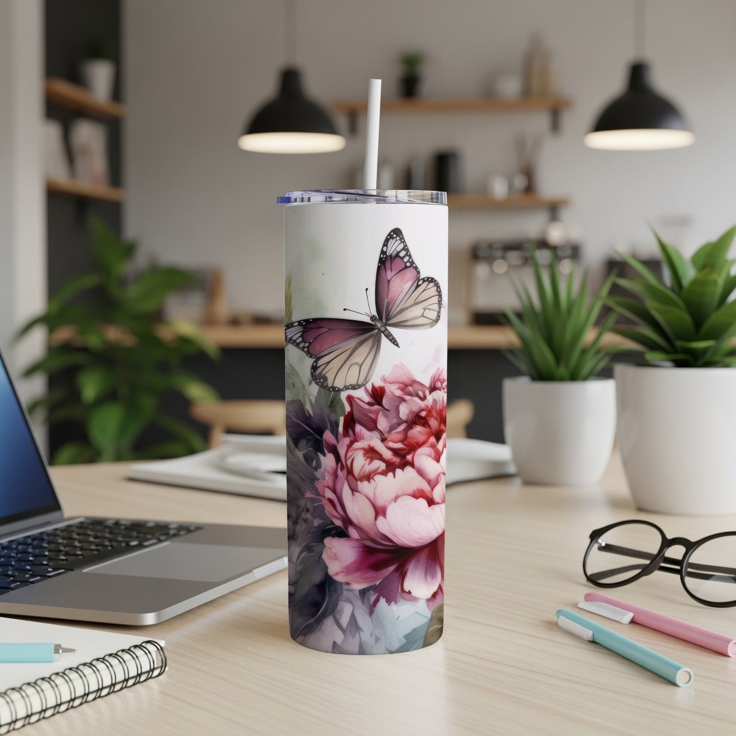 White tumbler with butterfly and floral design, on desk with laptop and pens.