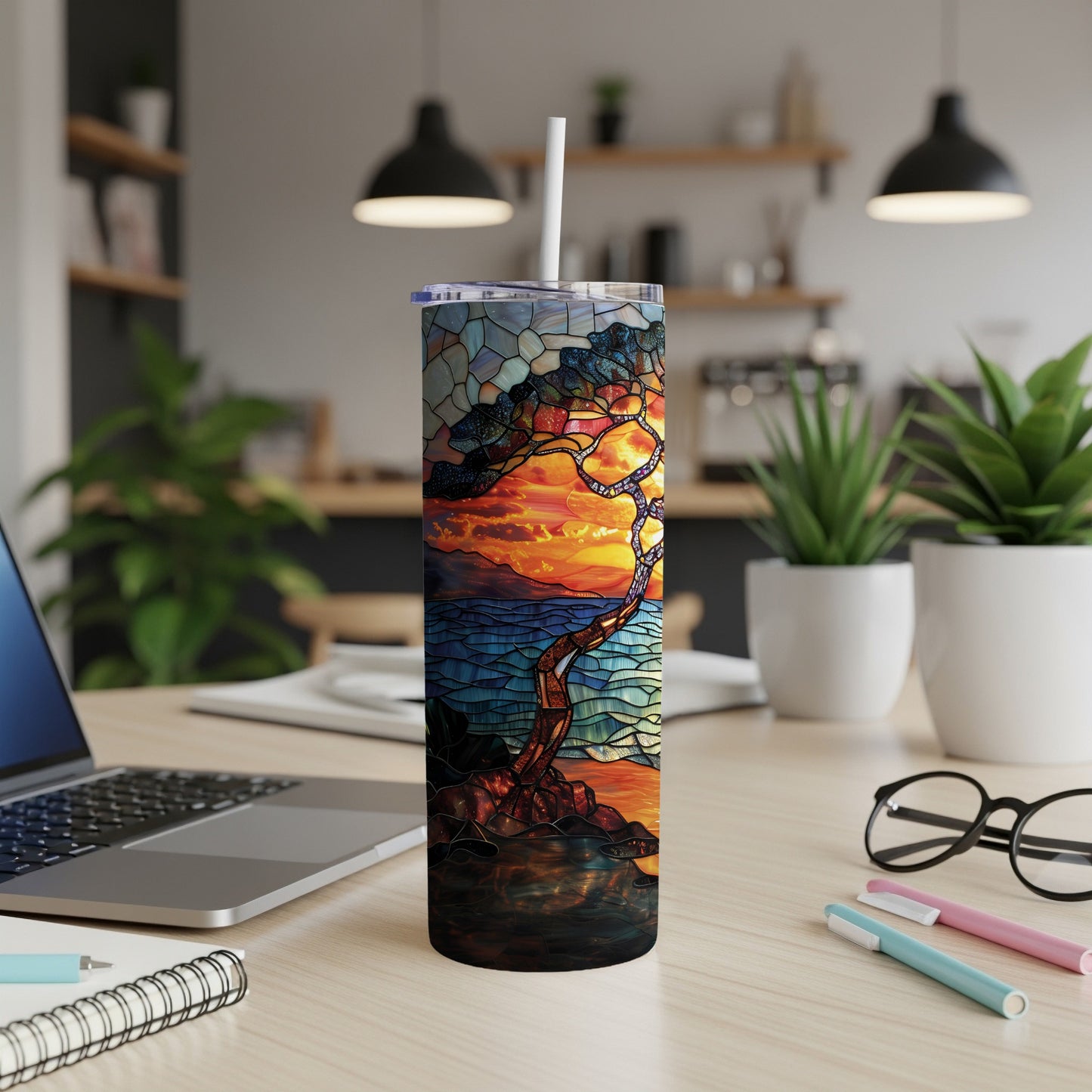 Stained glass tumbler with sunset tree scene on desk.