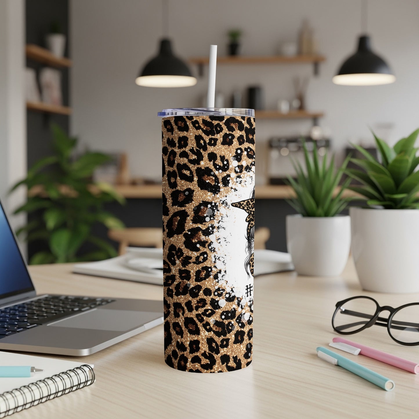 Leopard print tumbler with straw, laptop, and pens on desk.