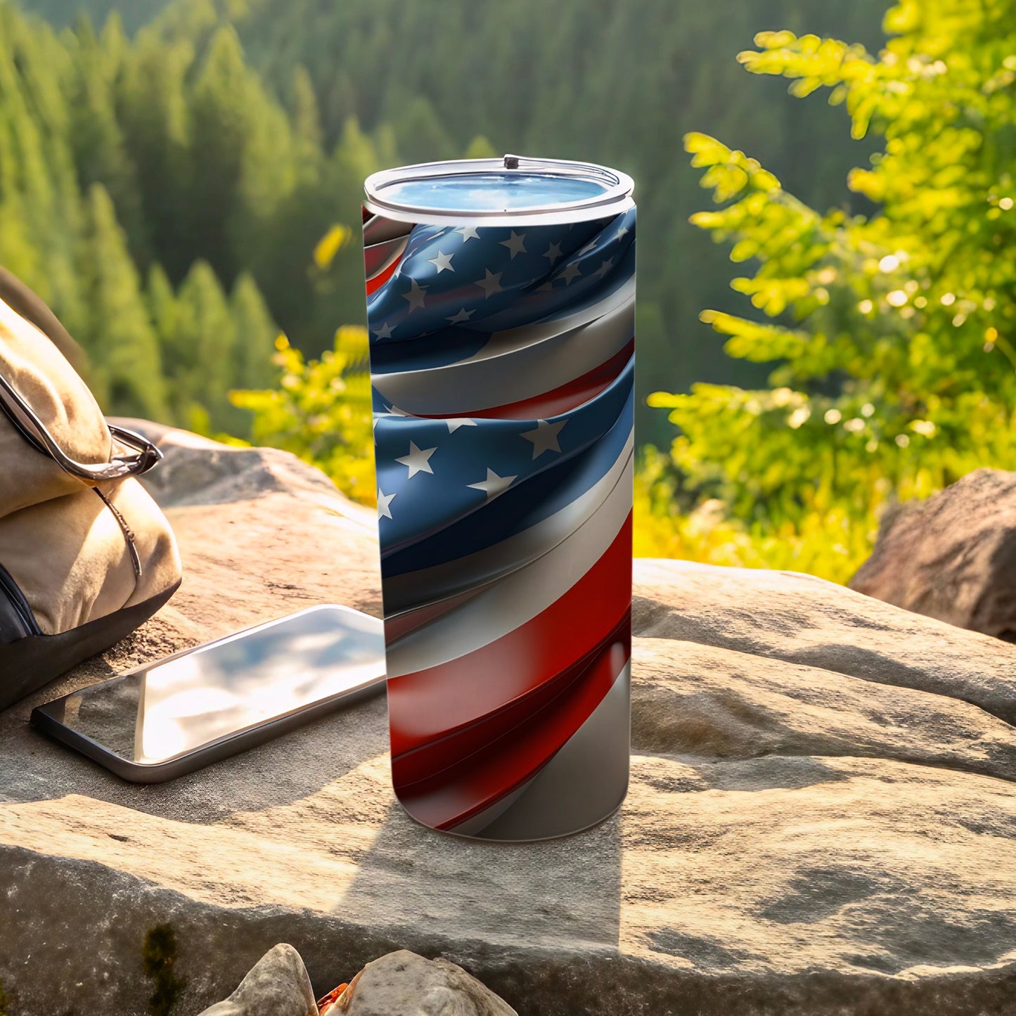 Tumbler with swirling American flag design rests on rock next to backpack and phone.