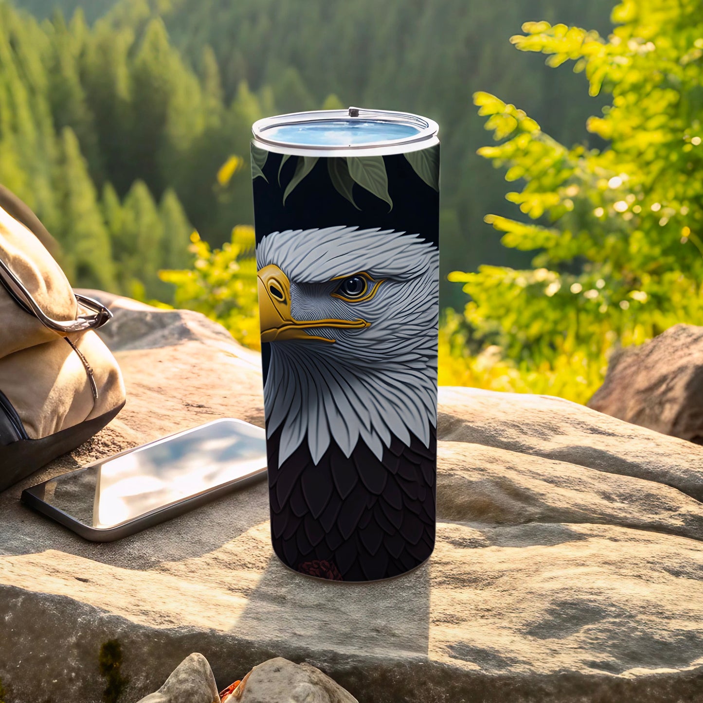 Tumbler with bald eagle design on a rock with phone and backpack.