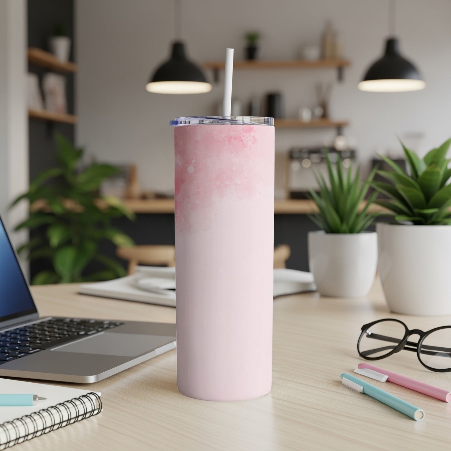 Pink watercolor tumbler with straw on desk next to laptop and pens.