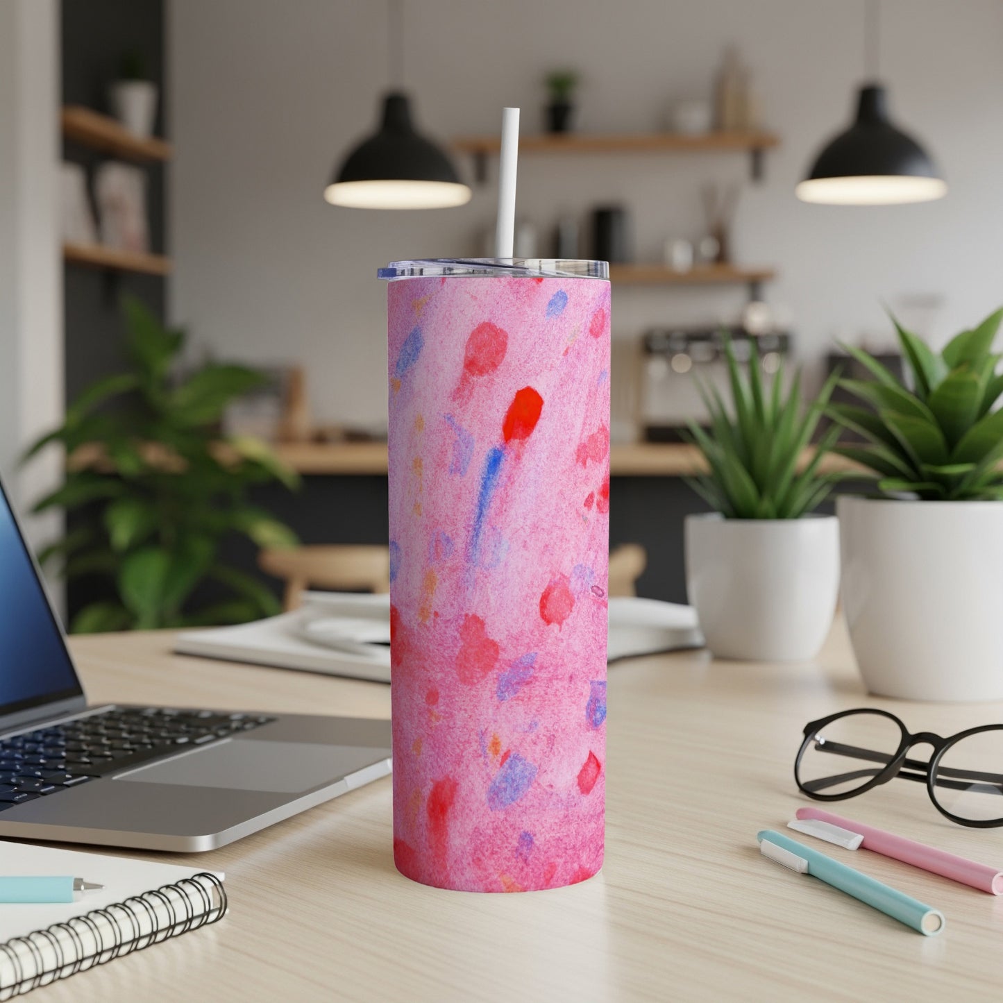 Pink and blue watercolor pattern tumbler with white lid and straw on desk.