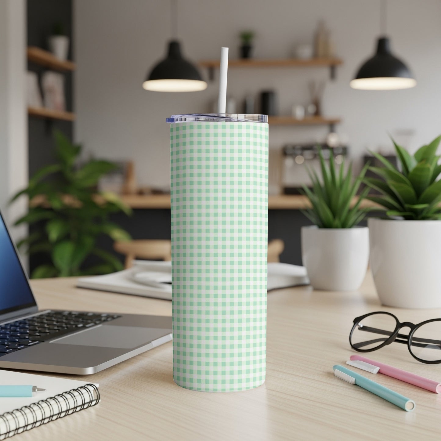 Mint green gingham pattern tumbler with white straw on a wooden desk.