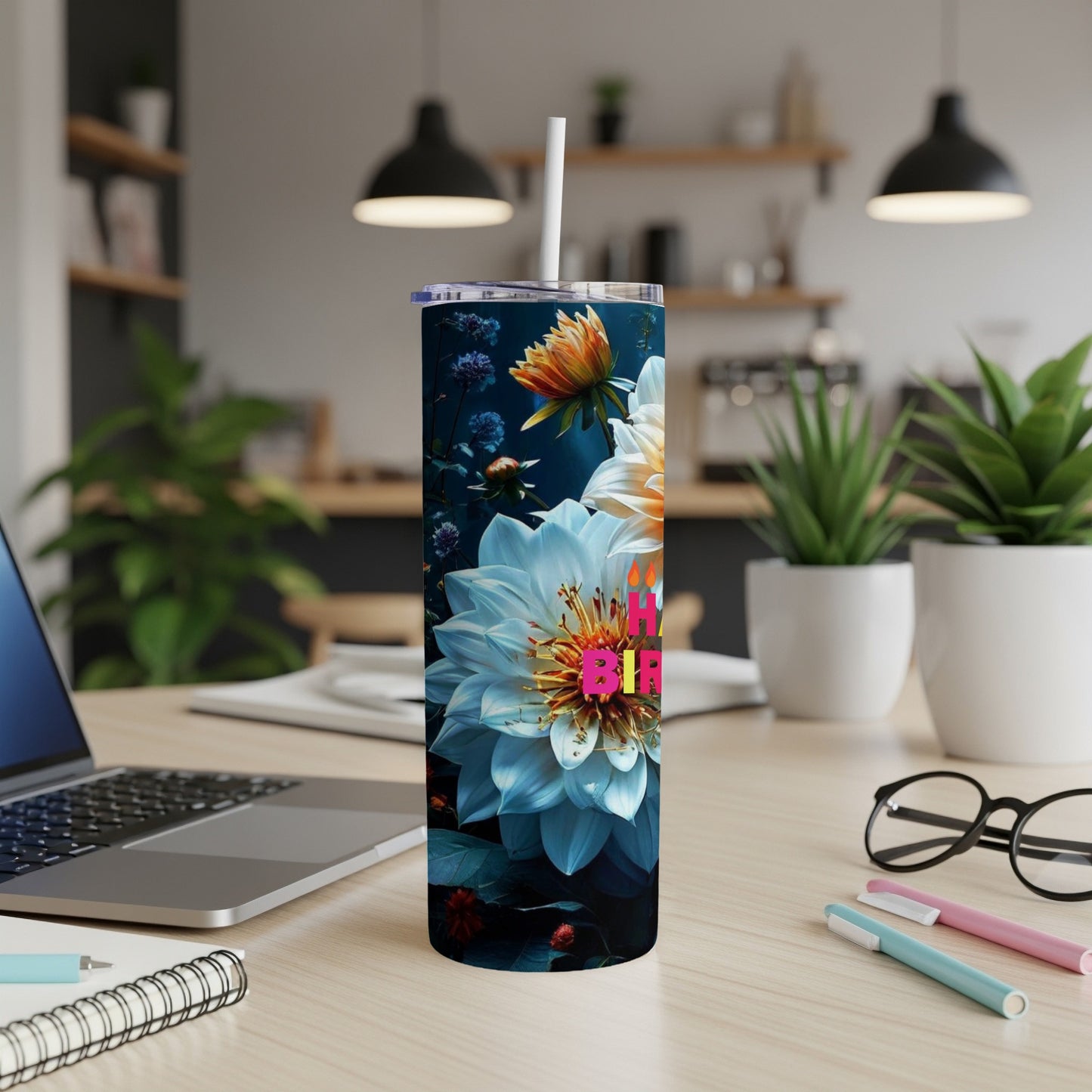 Floral tumbler with "Happy Birthday" text, on a desk with laptop and pens.