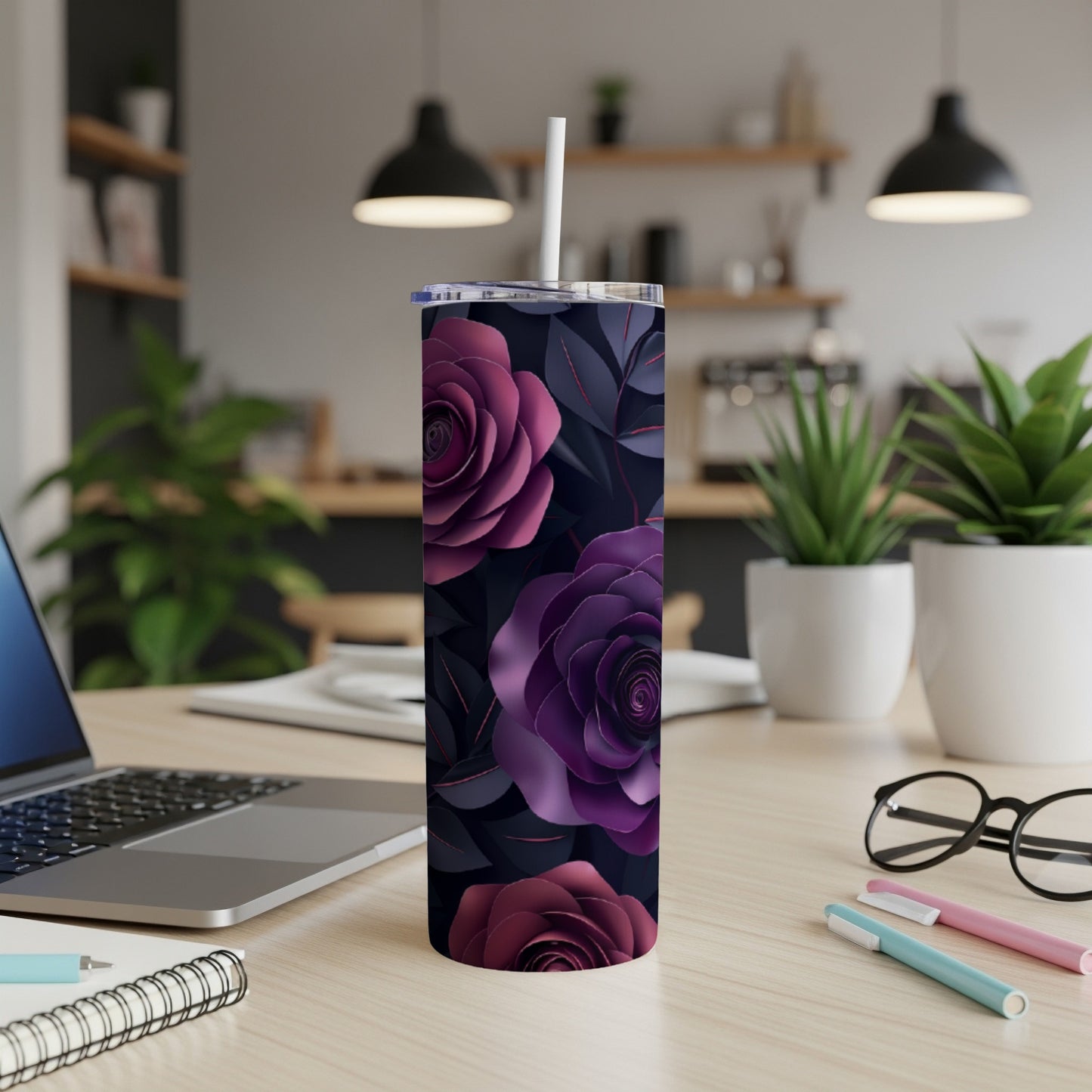 Purple floral tumbler with straw on a desk with a laptop and pens.