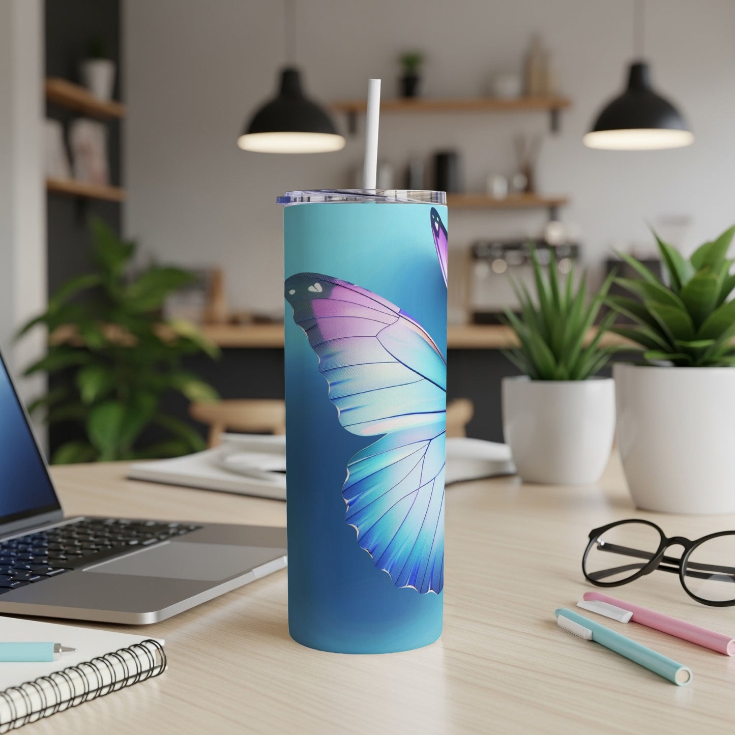 Blue and teal tumbler with butterfly wing design, straw, on desk.
