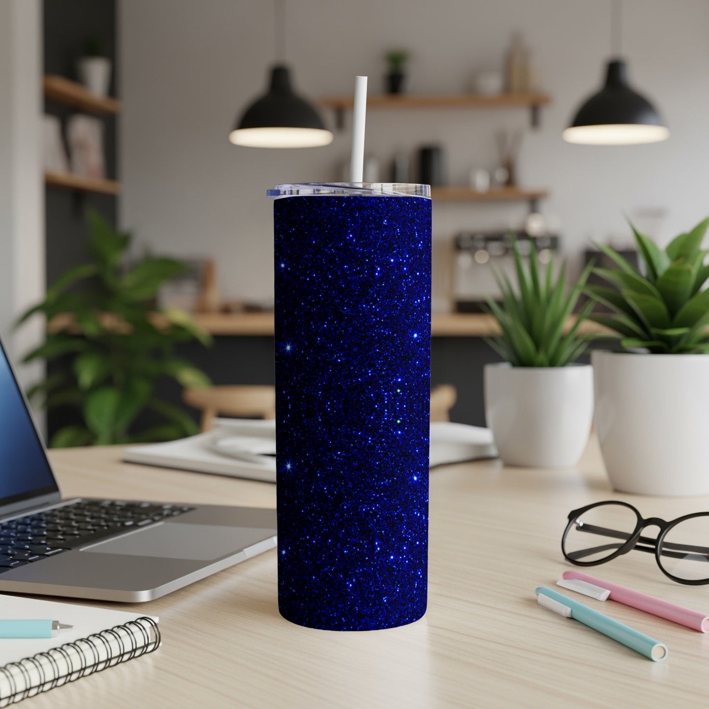 Sparkly blue glitter tumbler with a white straw on a desk.