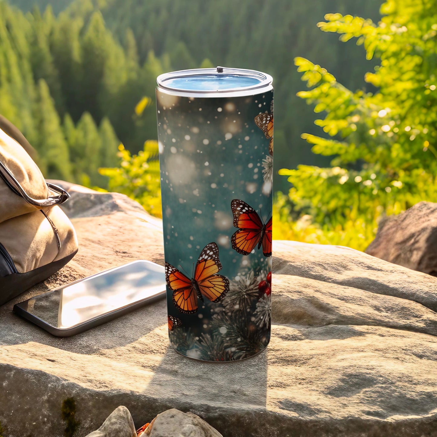Tumbler with monarch butterflies and pine branches on a rocky surface.