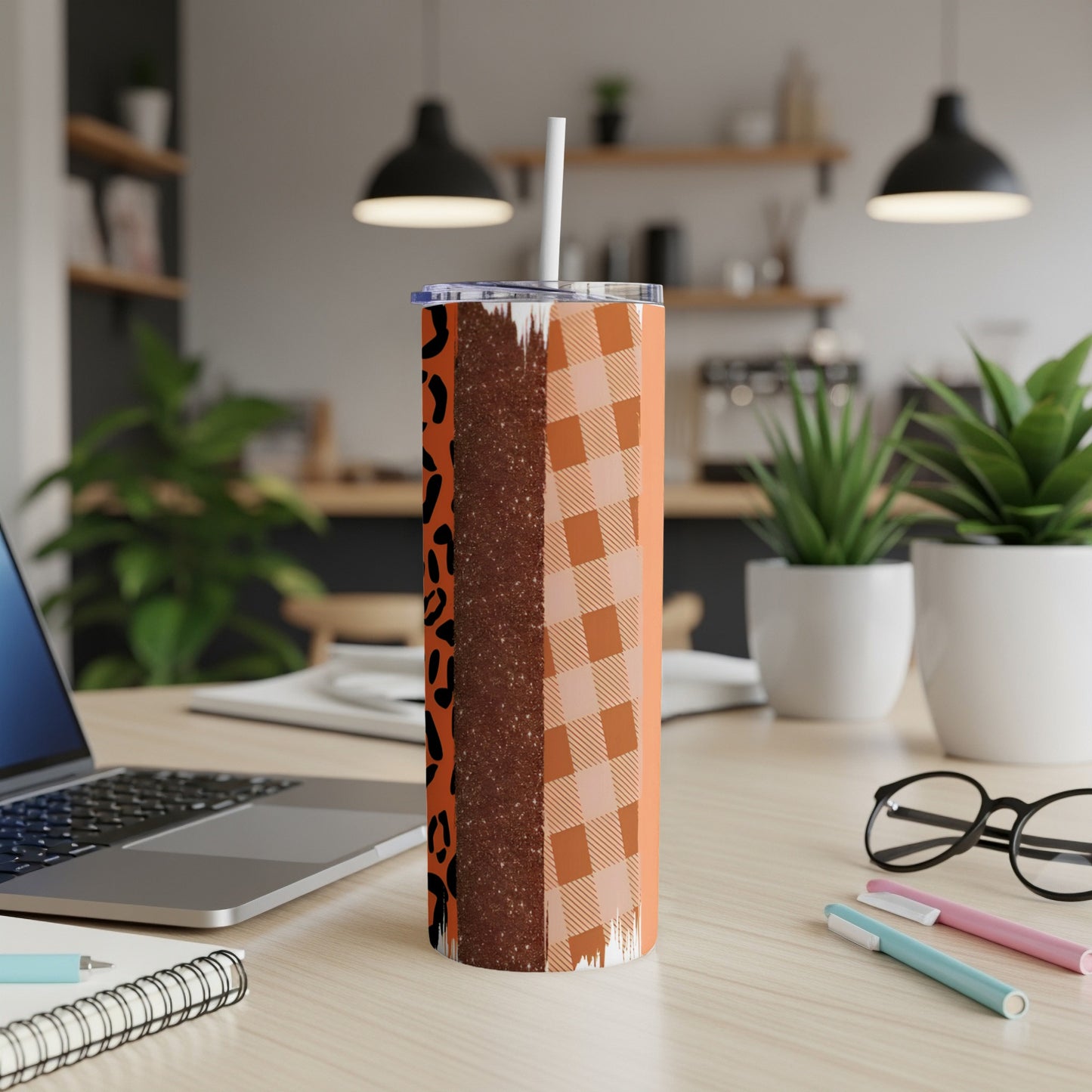 Orange plaid and leopard print tumbler with straw on a desk.