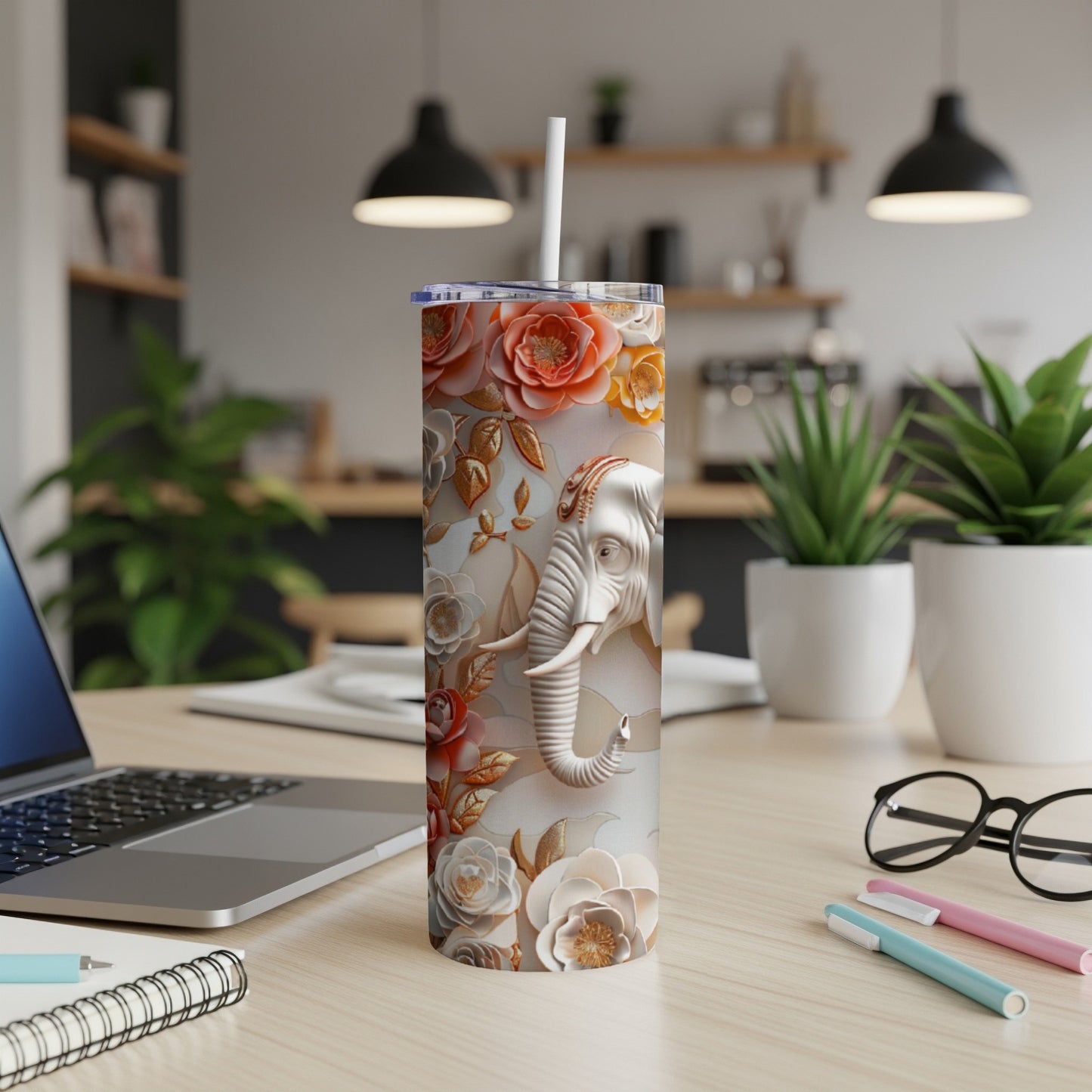 Floral elephant design on a white tumbler with a straw, on a desk.