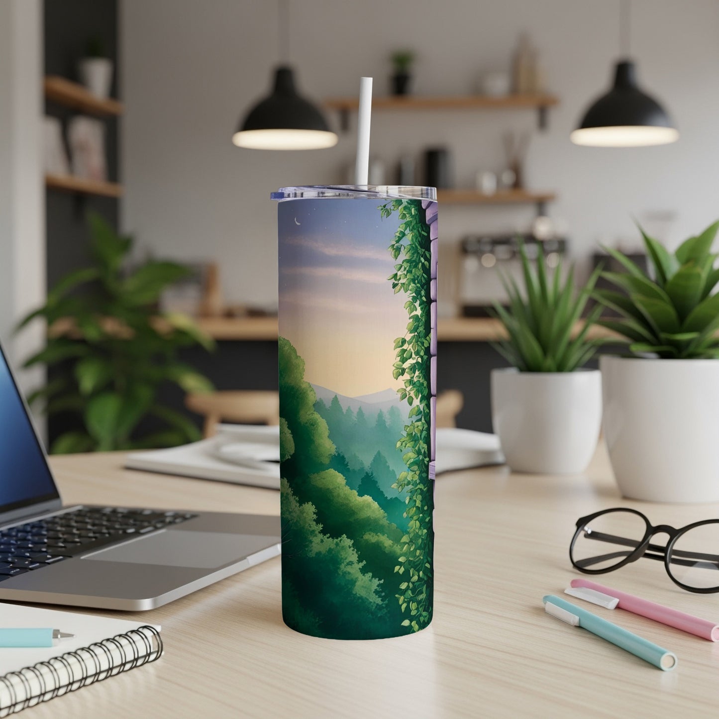 Tall tumbler with forest and sunset scene, on a desk.