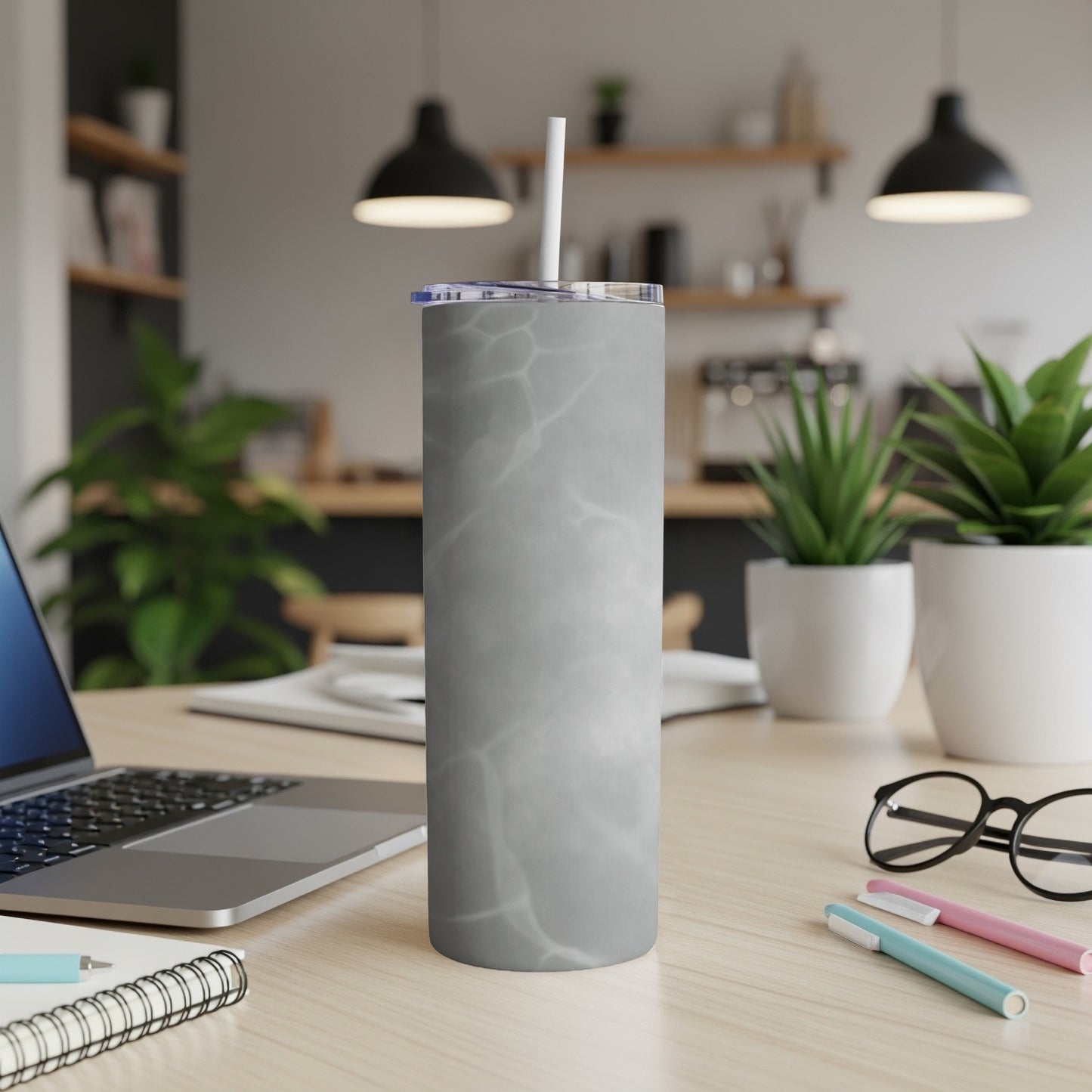 Gray marble pattern tumbler with straw on a wooden desk with laptop and plants.