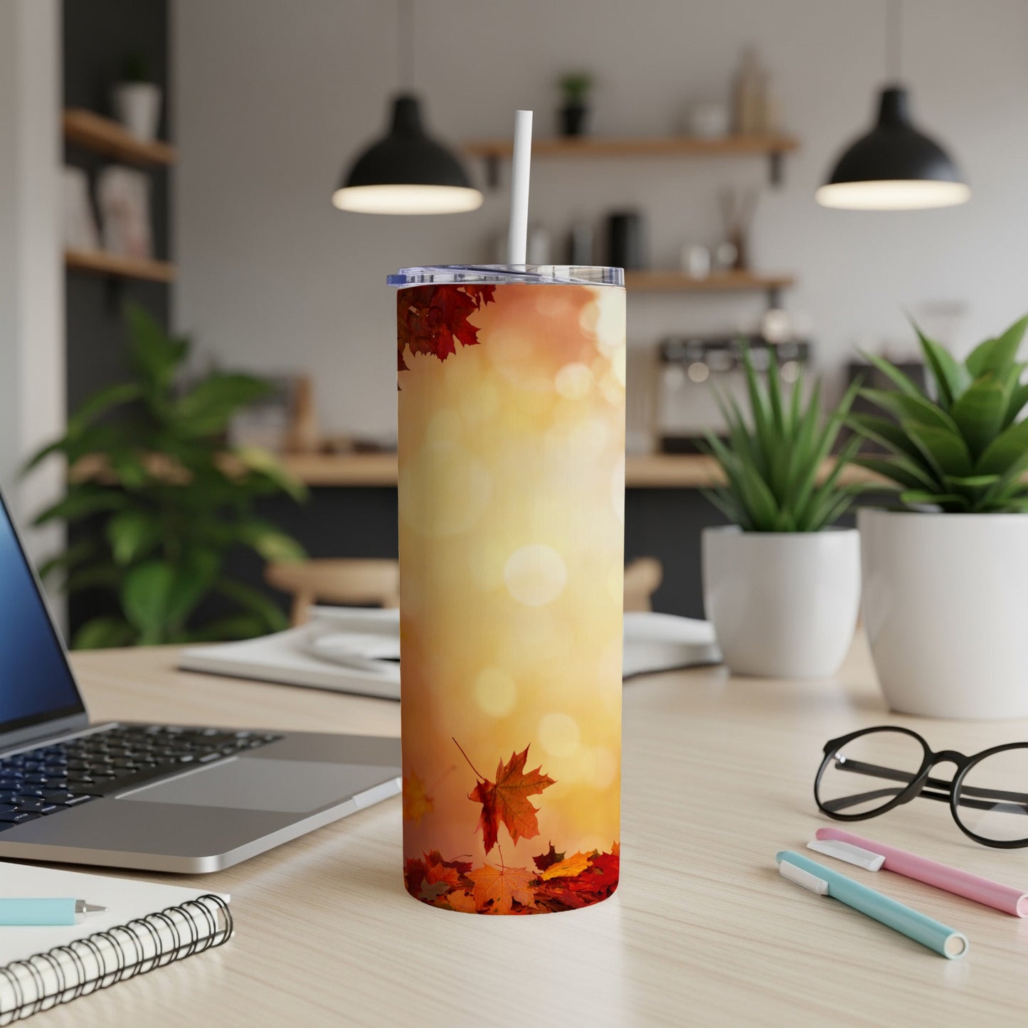 Fall leaves tumbler with straw on a desk next to a laptop.