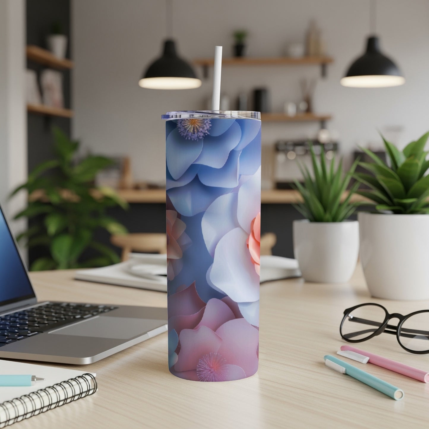 Floral patterned tumbler with a straw on a desk next to a laptop and pens.