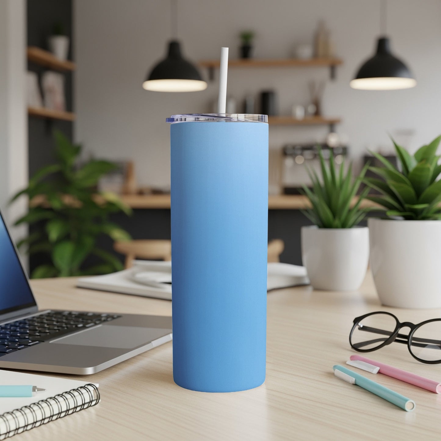 Blue stainless steel tumbler with straw on a desk next to a laptop.