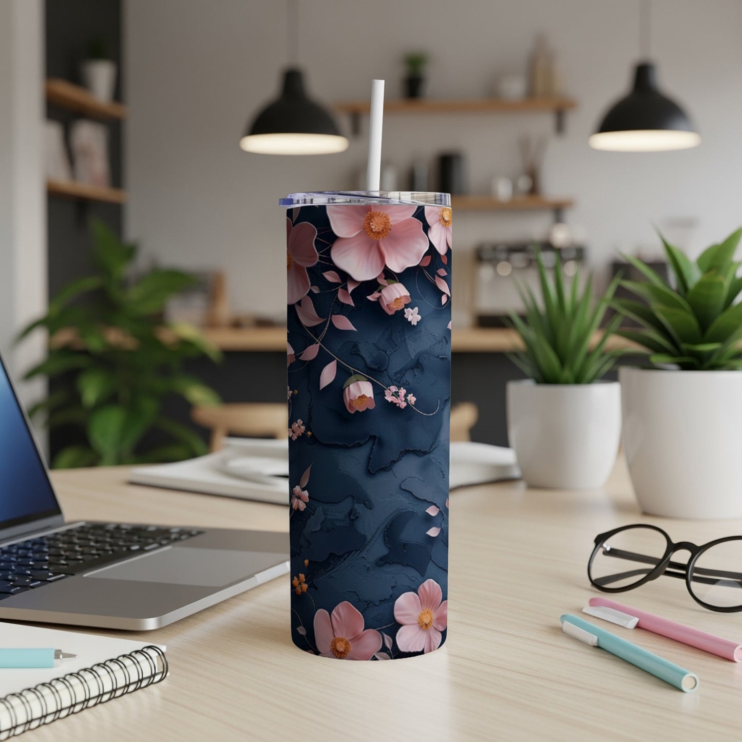 Floral navy tumbler with straw on a desk, next to a laptop.