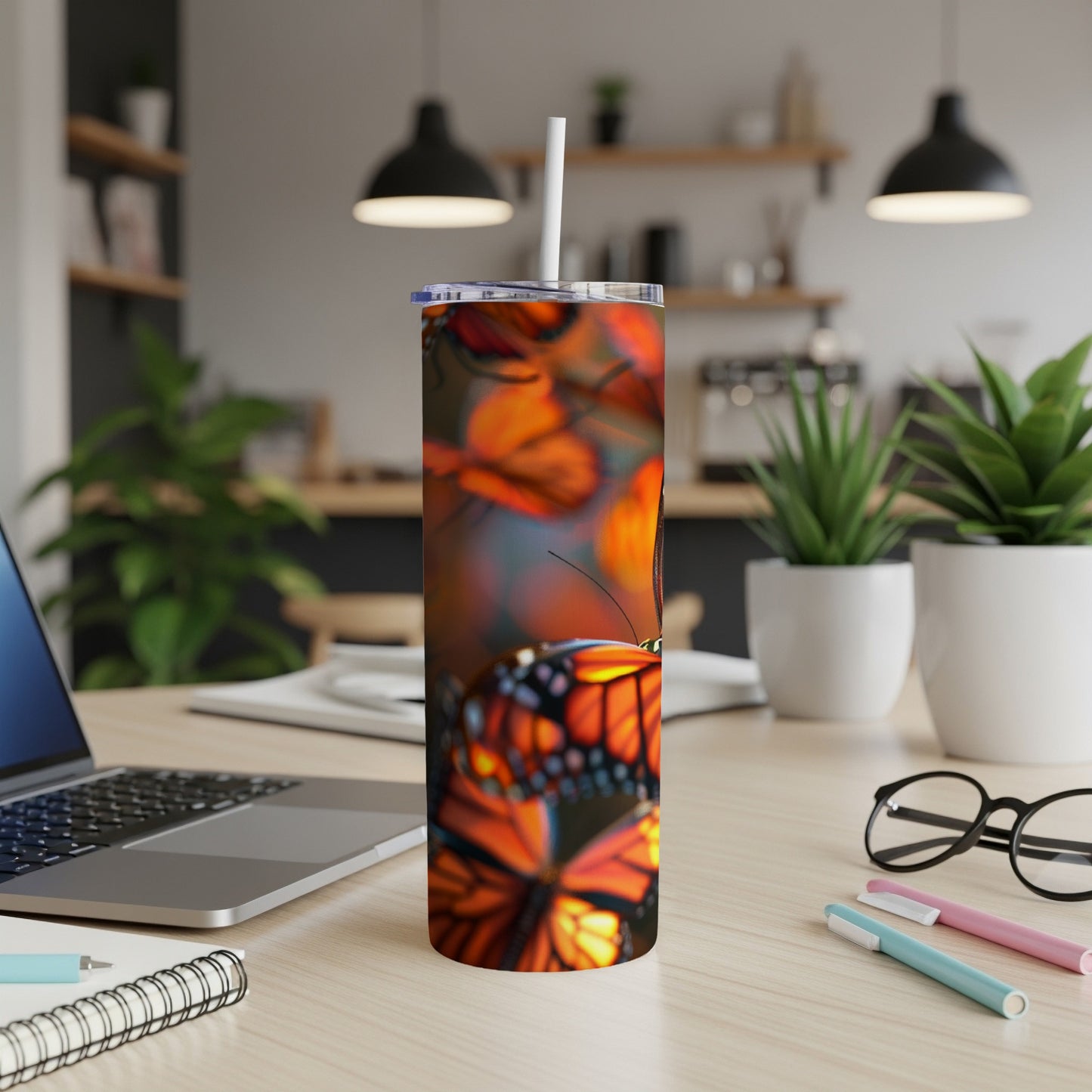 Tumbler with monarch butterflies and flowers, straw inserted, on a desk.