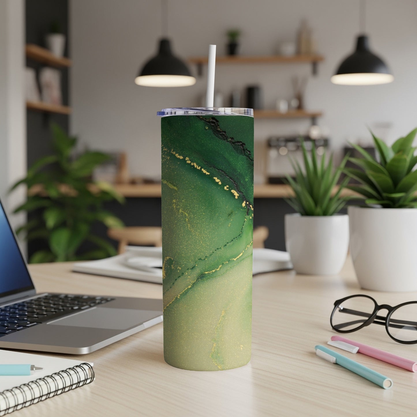 Green and gold marble patterned tumbler with straw on a wooden desk.