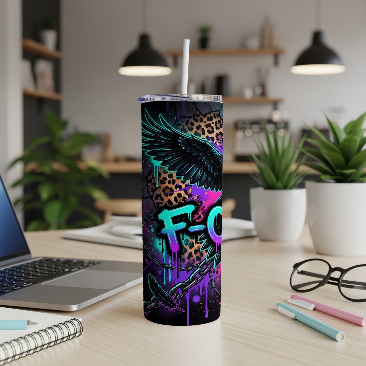 Black skinny tumbler with eagle, feathers, and graffiti text "FCK" on a desk.