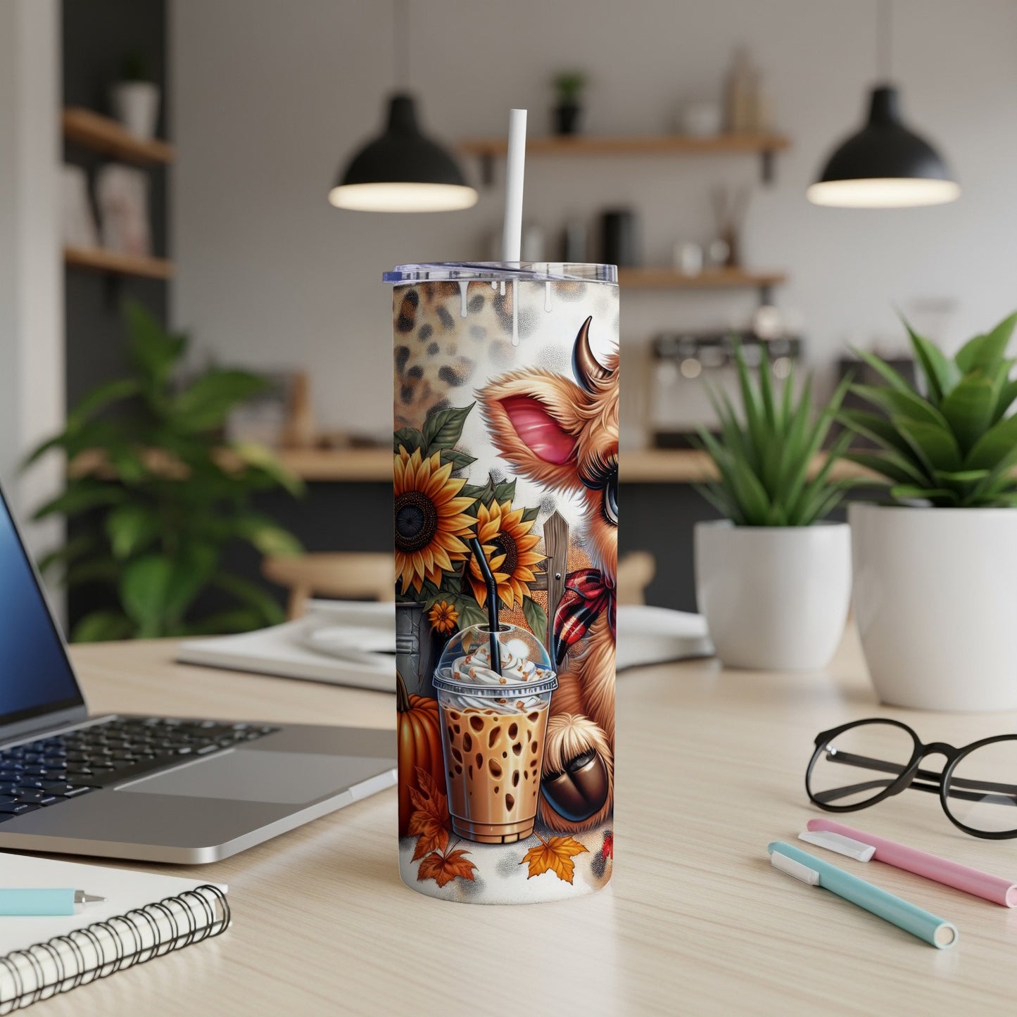 Cow and sunflower tumbler with latte, straw, and autumn leaves.