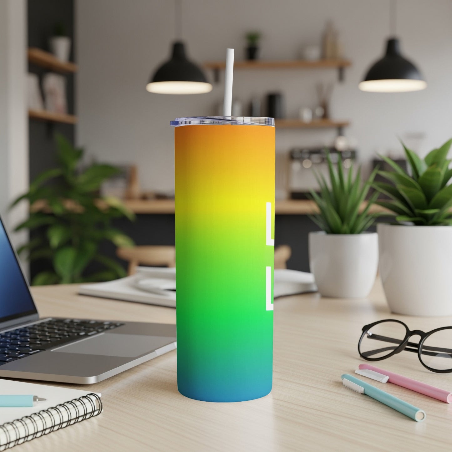 Rainbow gradient tumbler with straw on a desk with a laptop and office supplies.
