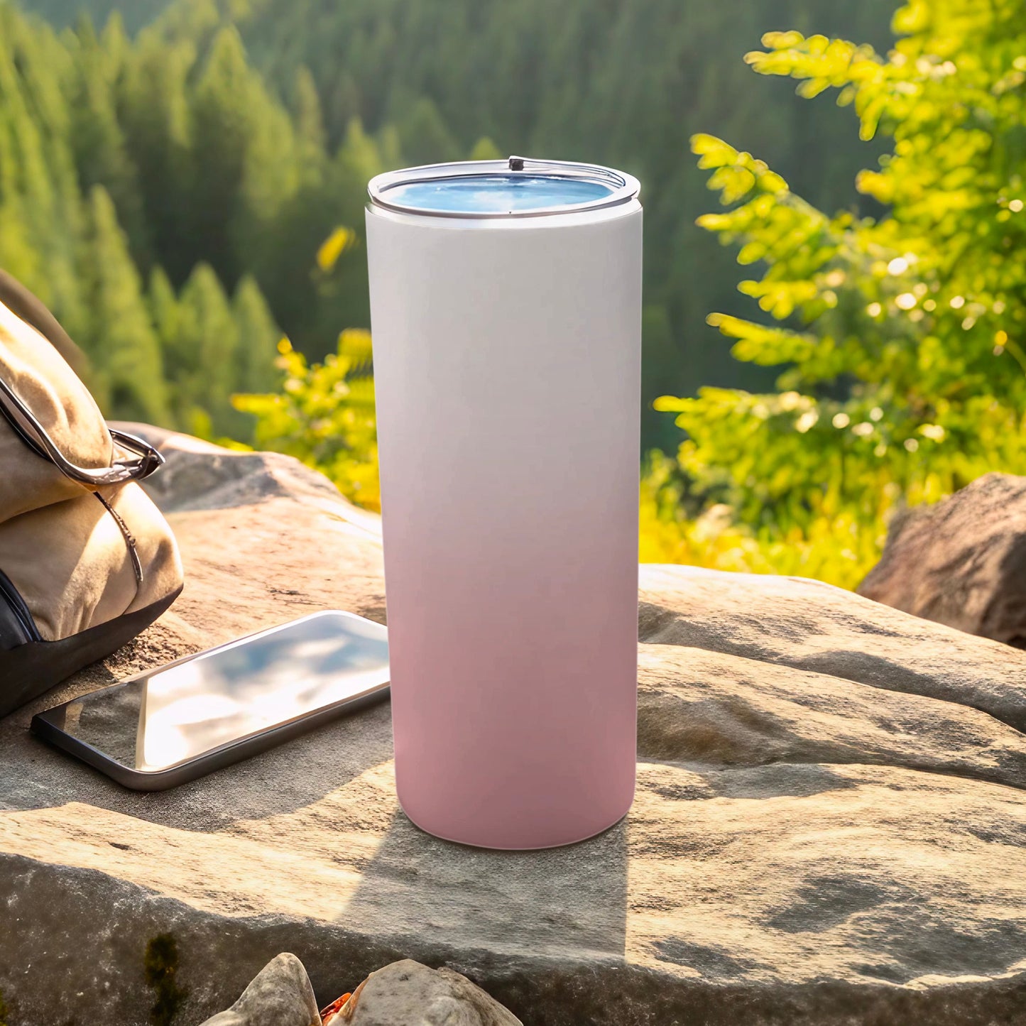 White and pink ombre tumbler with lid on rock, phone and backpack nearby.