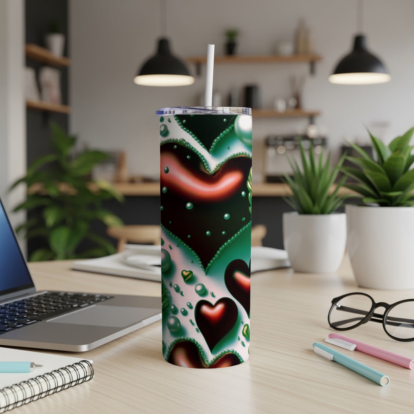 Tall tumbler with a heart pattern and straw, on a desk.