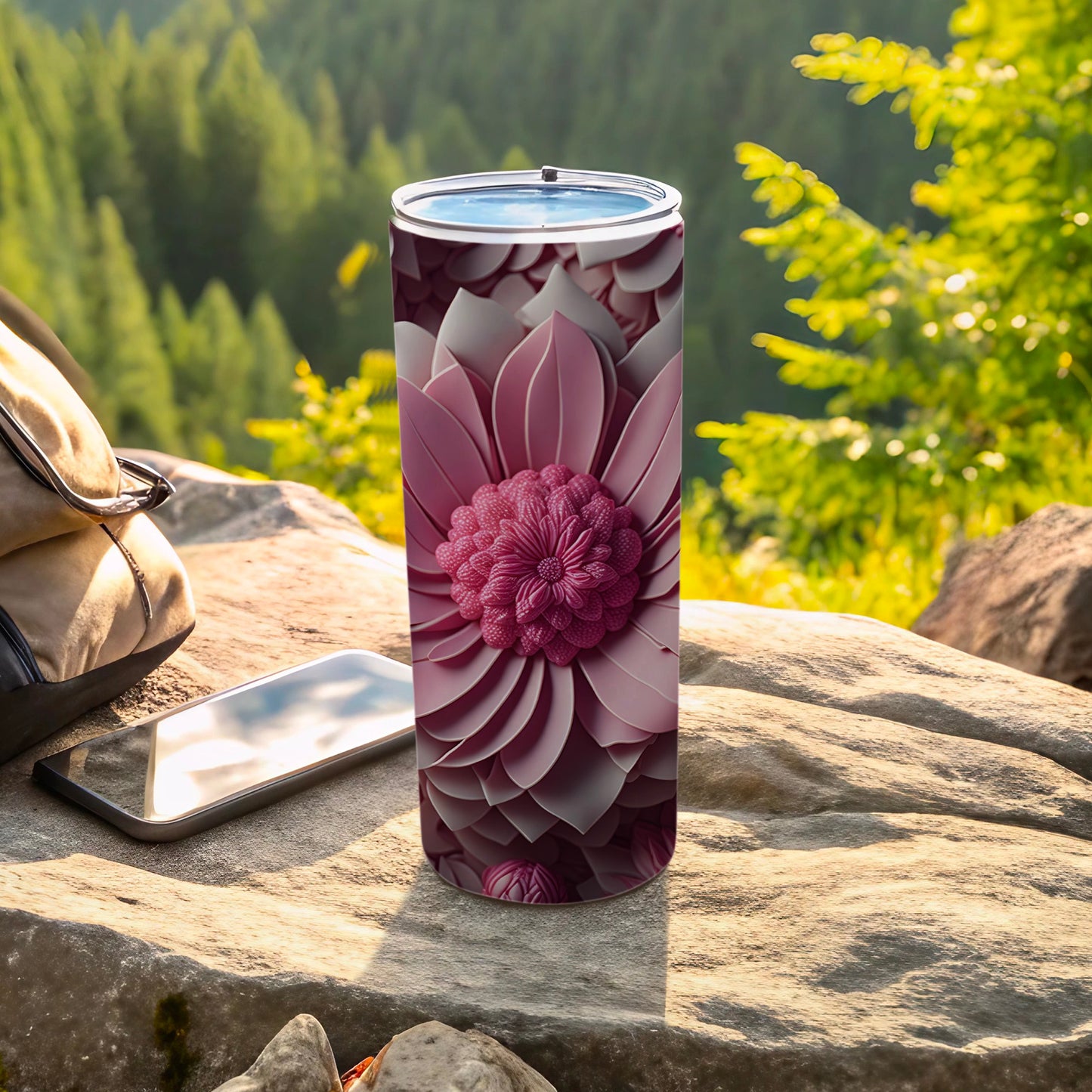 Pink floral tumbler on rock with backpack and phone outdoors.