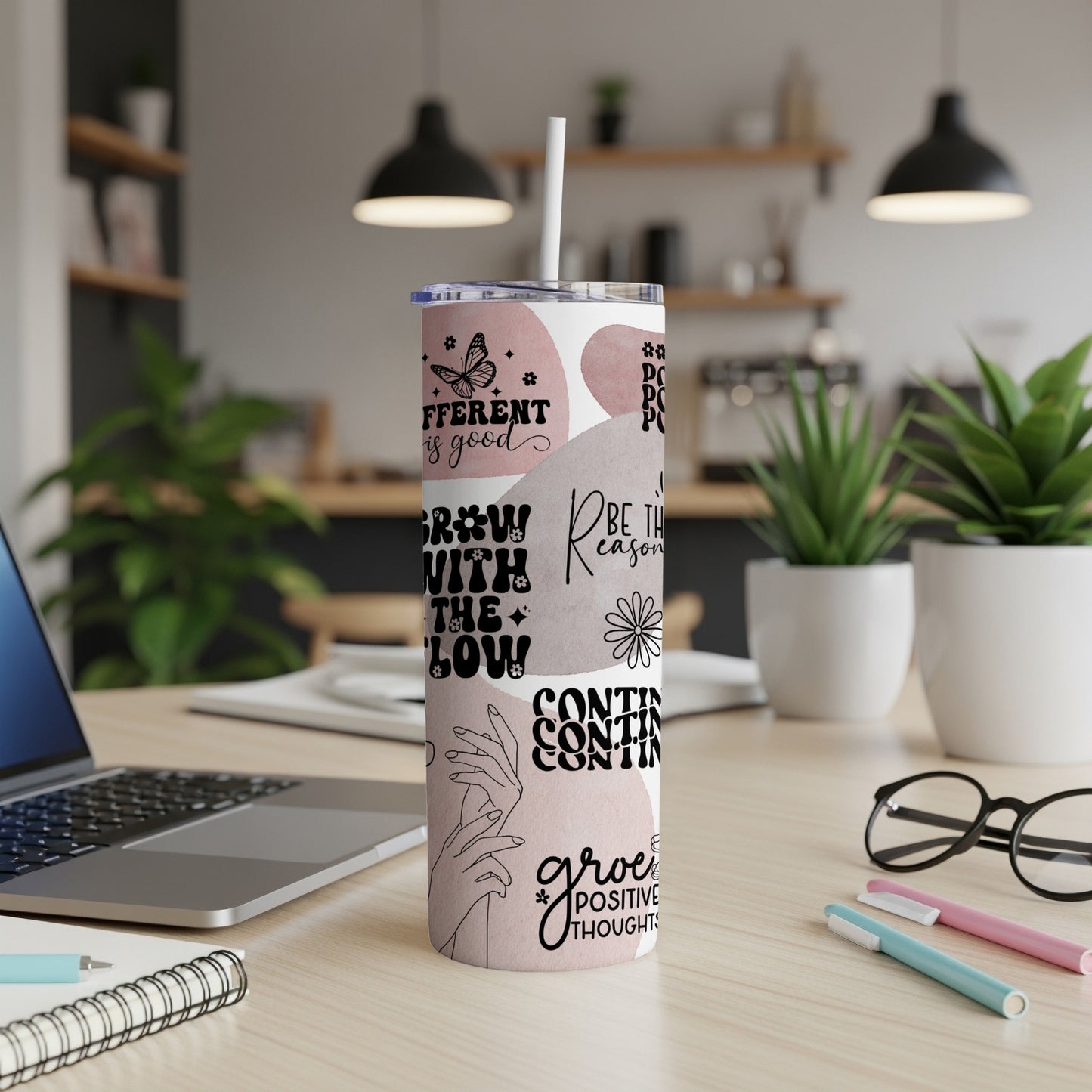 Tumbler with positive affirmations and floral designs on a desk.