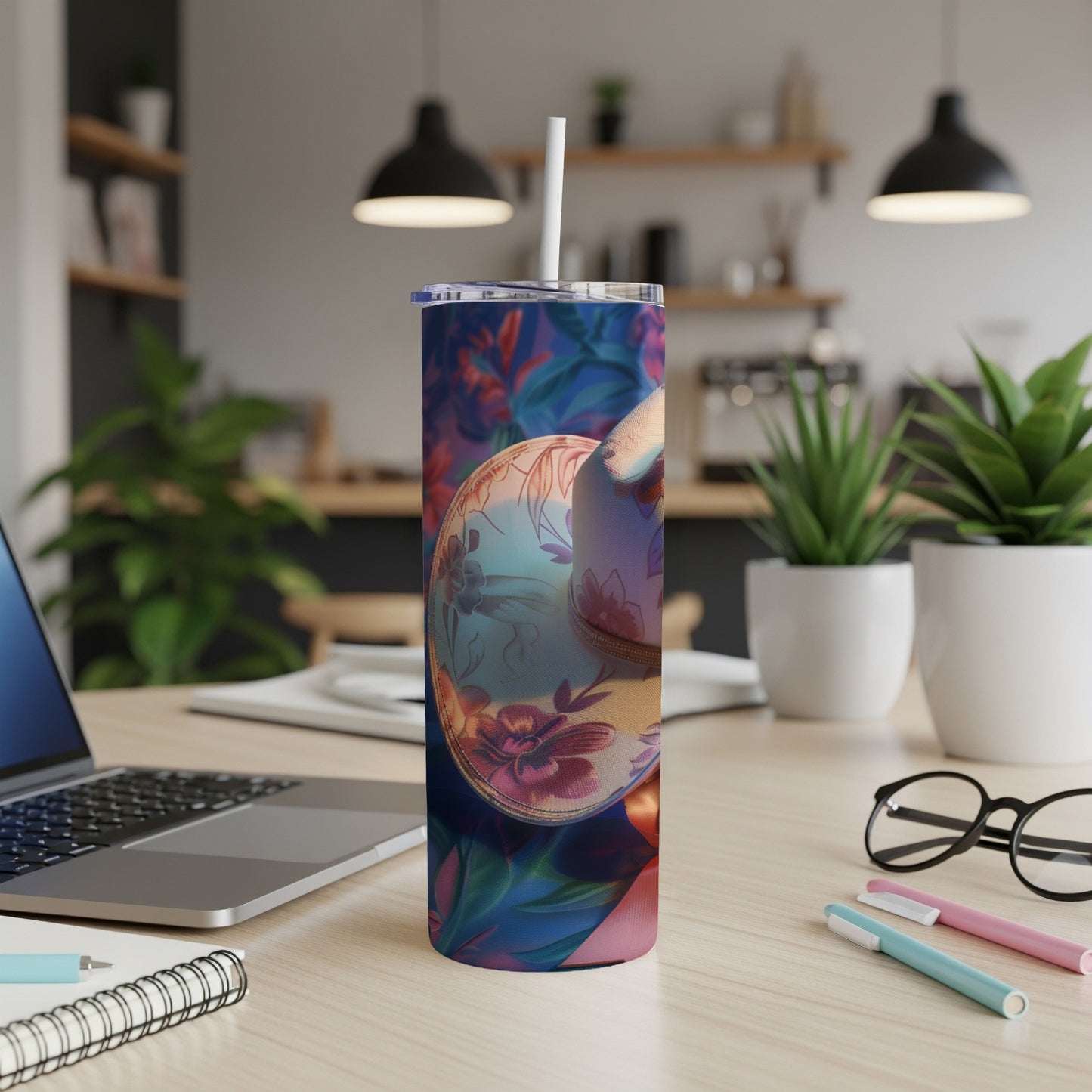 Floral tumbler with straw on desk next to laptop and supplies.