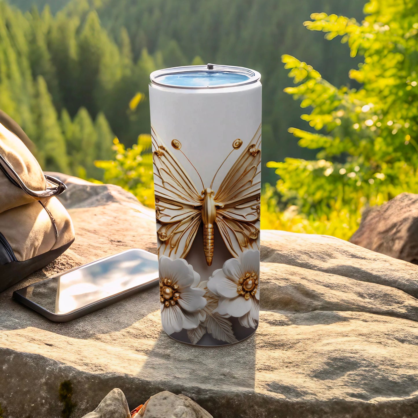 White tumbler with gold butterfly and floral design on rocky surface.