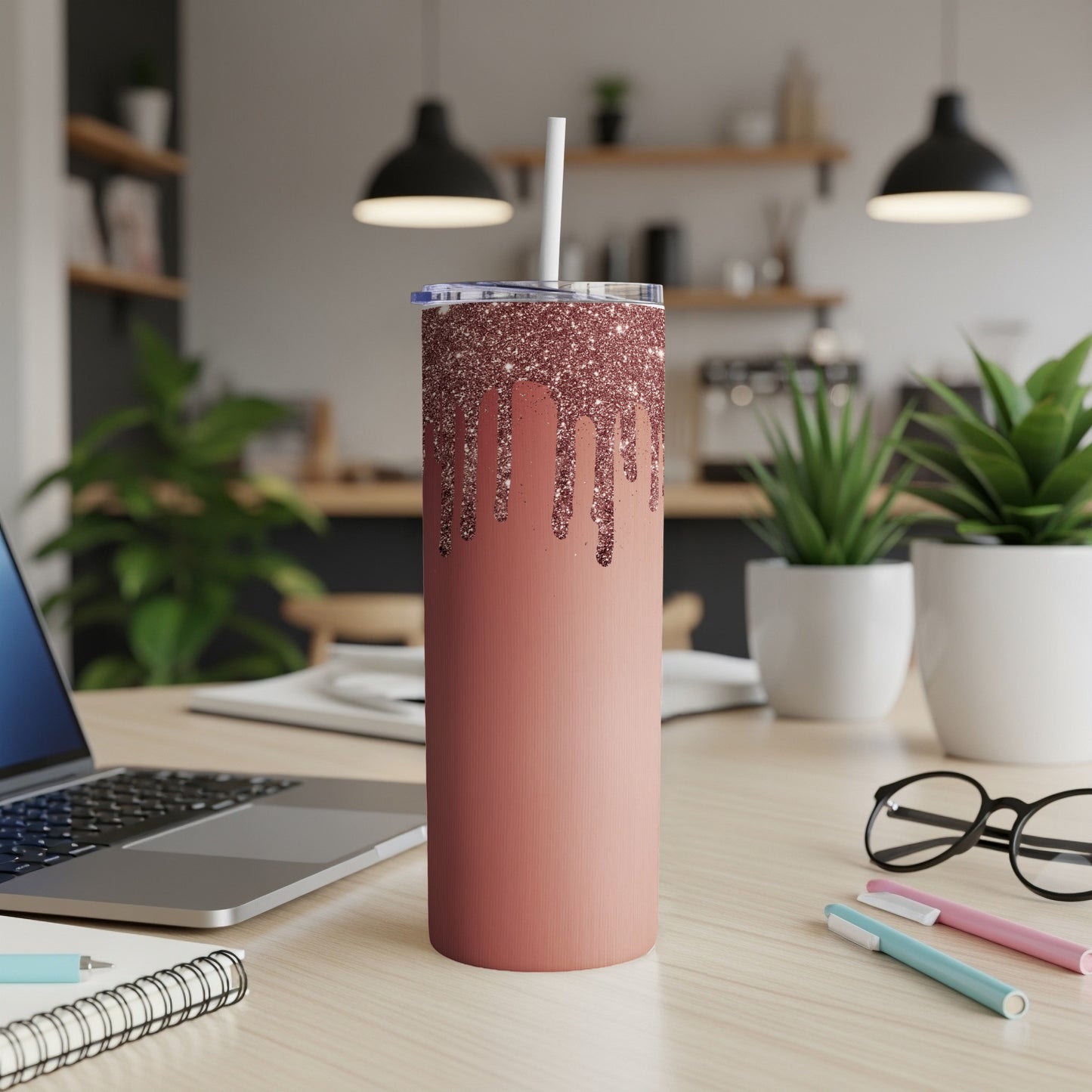 Rose gold glitter drip tumbler with straw on a desk.