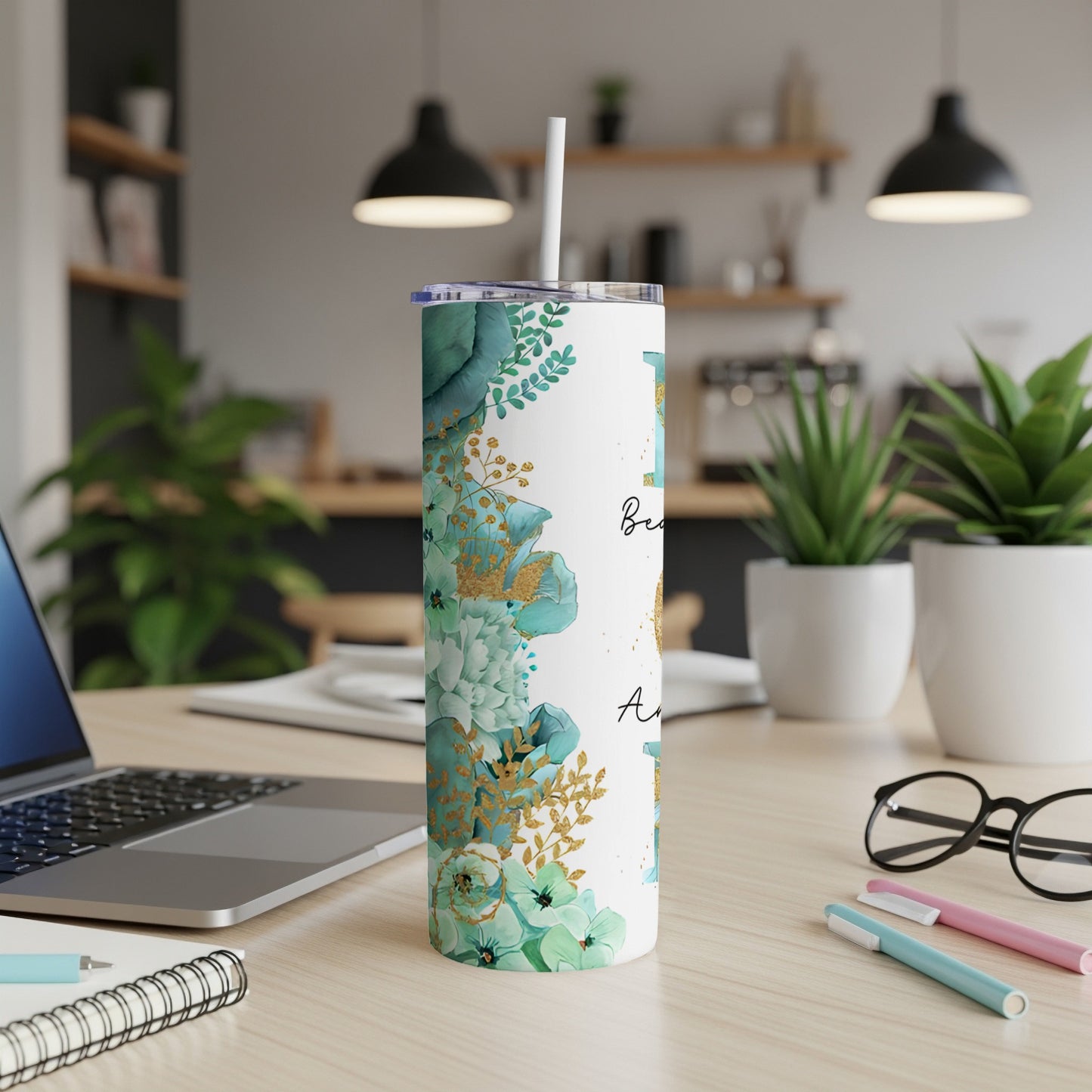 Floral tumbler with straw on desk next to laptop and pens.