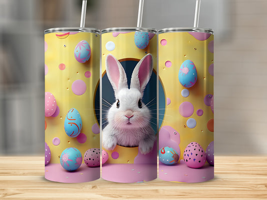 Easter bunny peeking from yellow tumbler with colorful eggs.