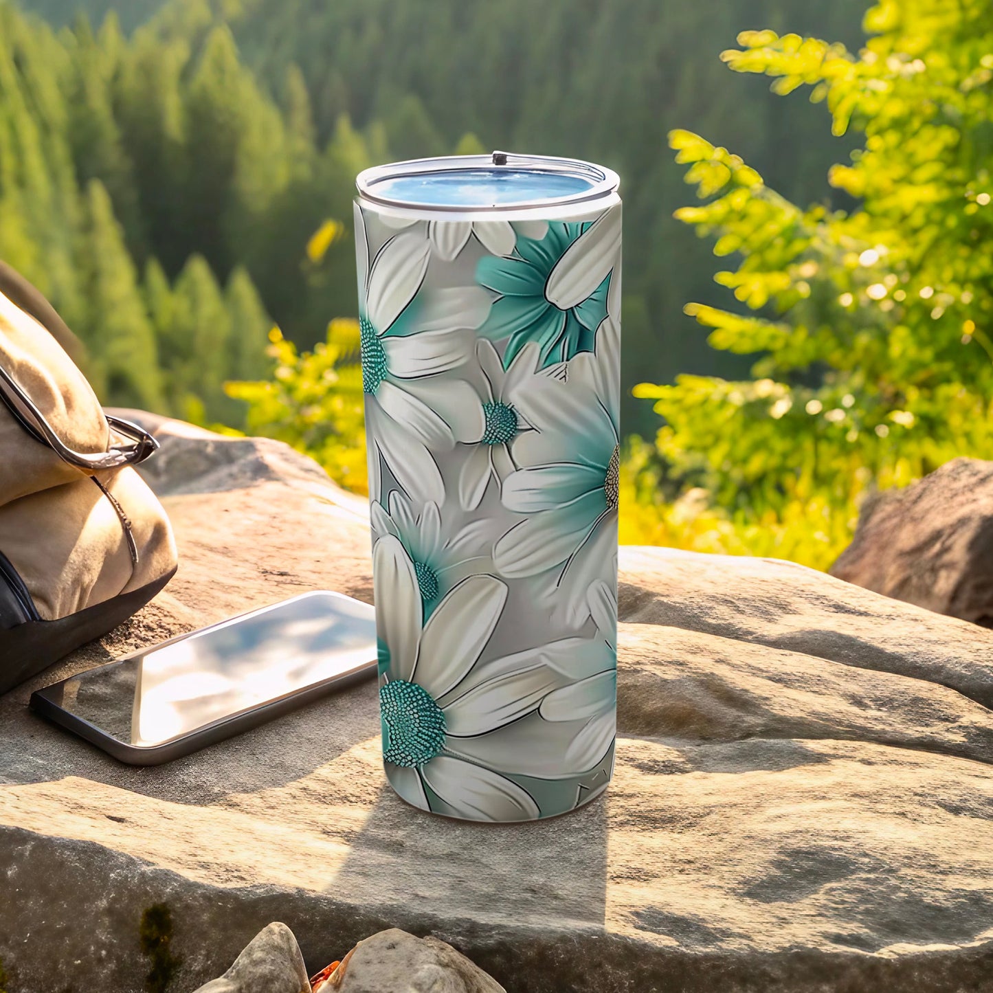 Floral tumbler with green flowers, resting on rocks with a backpack and phone.